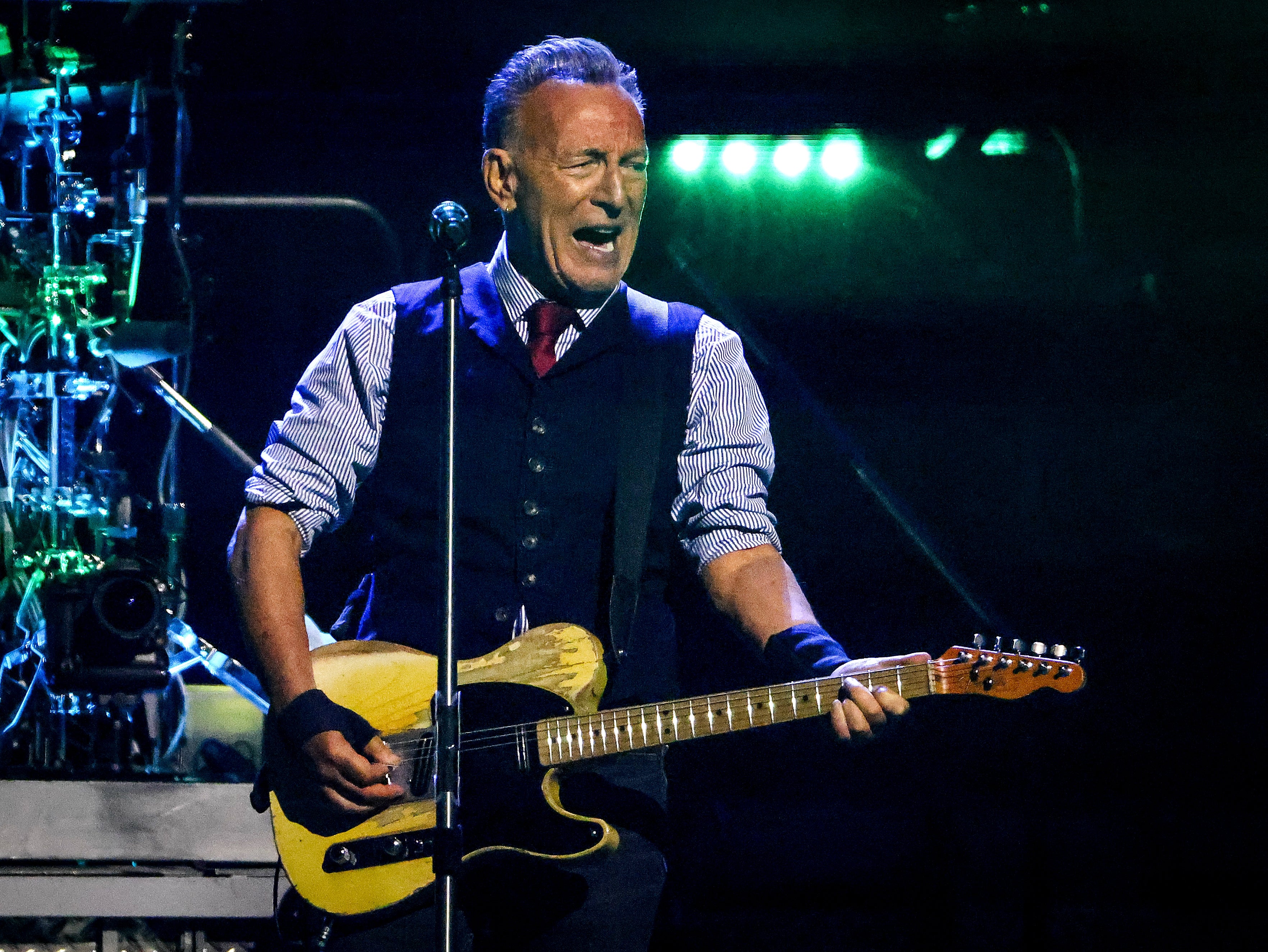 Musiker som lidenskapelig opptrer på scenen med en gitar, iført vest over stripet skjorte og slips