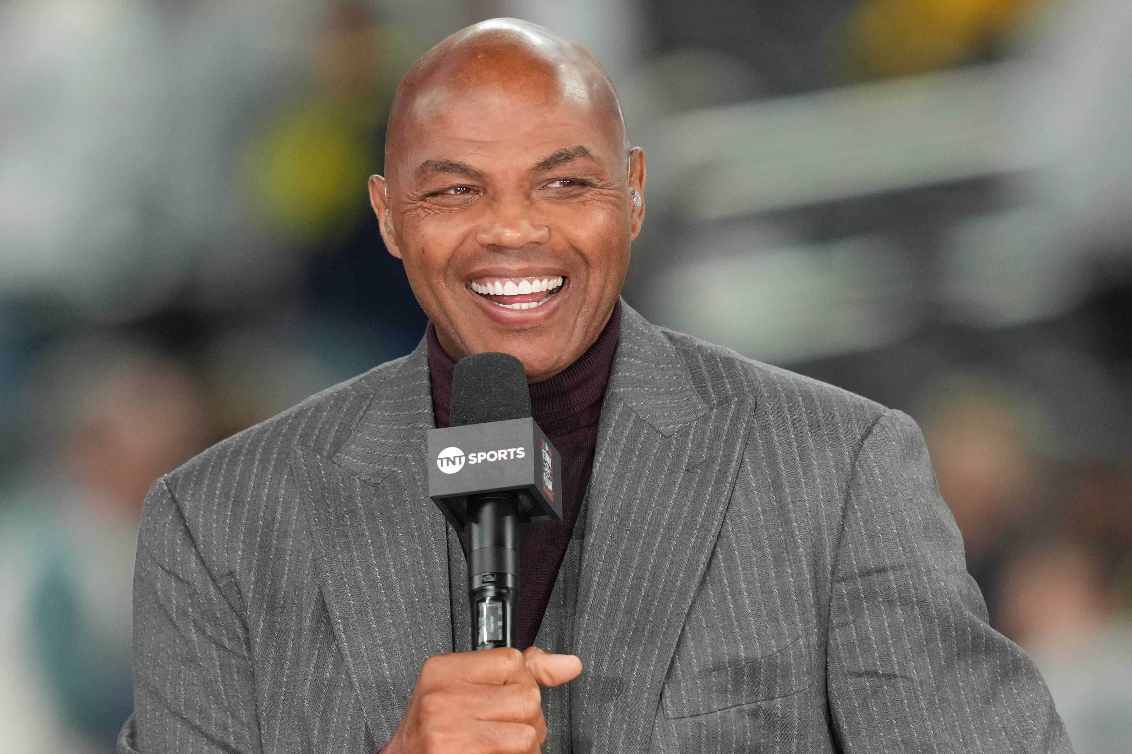 Person som smiler og holder en mikrofon, iført dress, ser ut til å være engasjert i en sending eller intervju