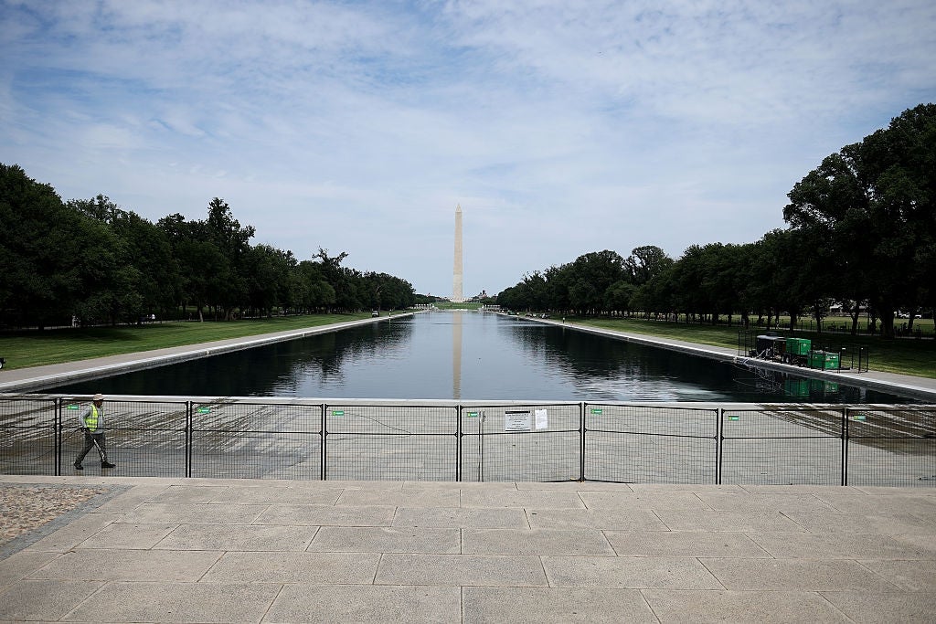 Reflekterende basseng og Washington-monumentet i det fjerne på en klar dag, med en person som går forbi og konstruksjonsbarrierer i forgrunnen