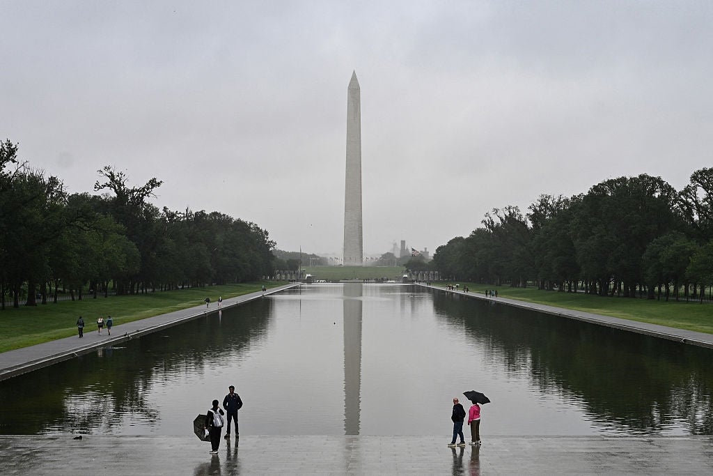 Folk med paraplyer går langs det reflekterende bassenget foran Washington-monumentet på en overskyet dag