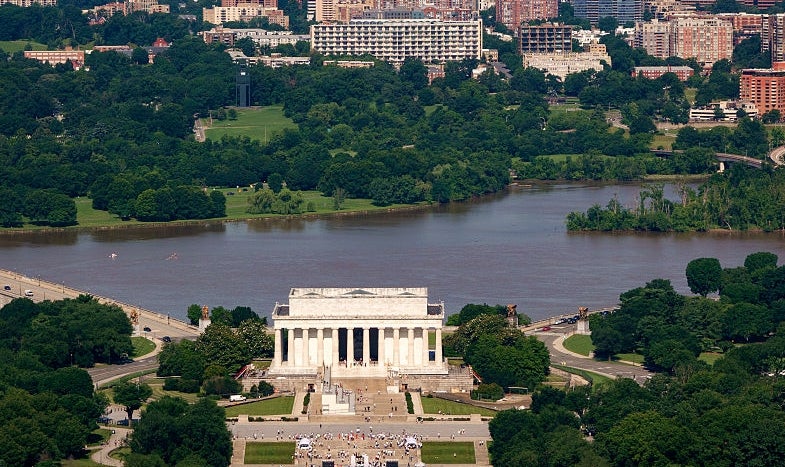 Luftfoto av Lincoln Memorial med reflekterende basseng, omgitt av trær, bybilde i bakgrunnen