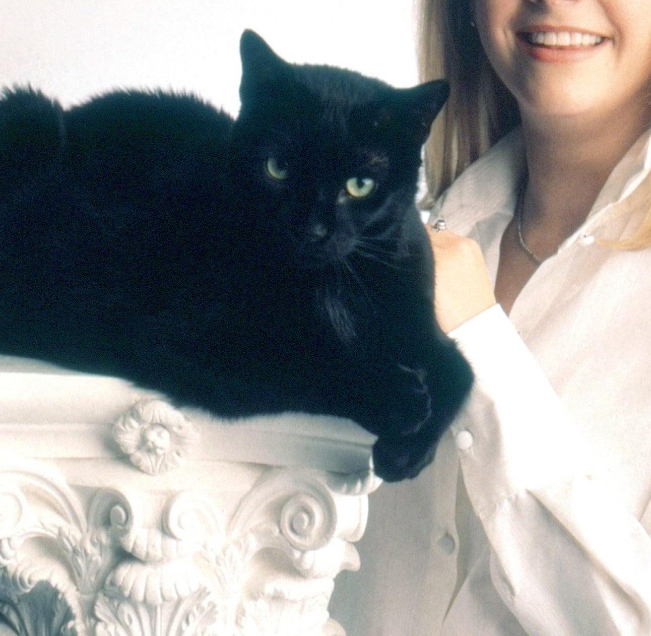 Person successful  achromatic  outfit with a achromatic  feline  connected  a decorative pillar, some  looking astatine  the camera