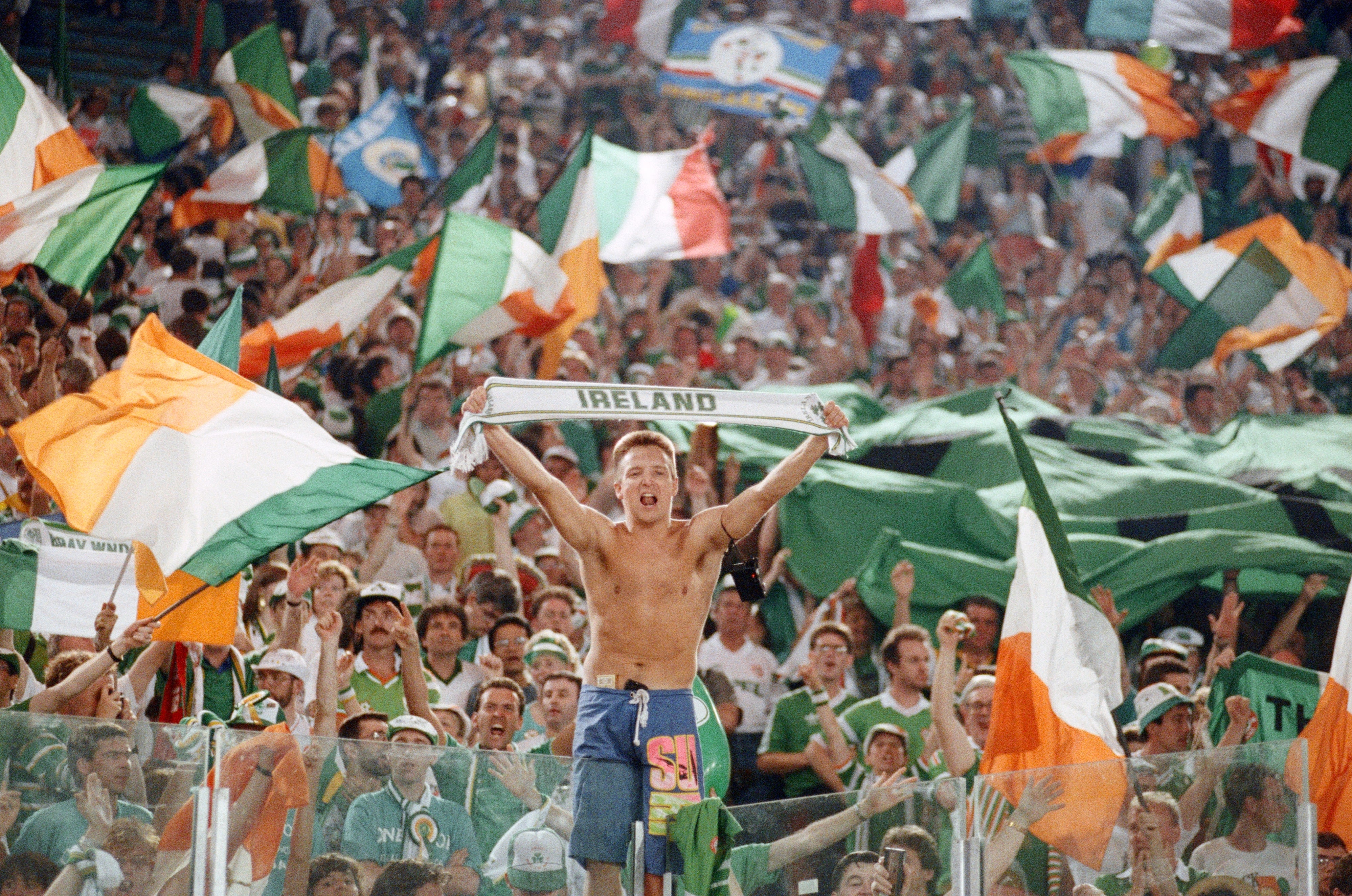 Soccer instrumentality successful a stadium holds an "Ireland" scarf, surrounded by cheering assemblage waving Irish flags