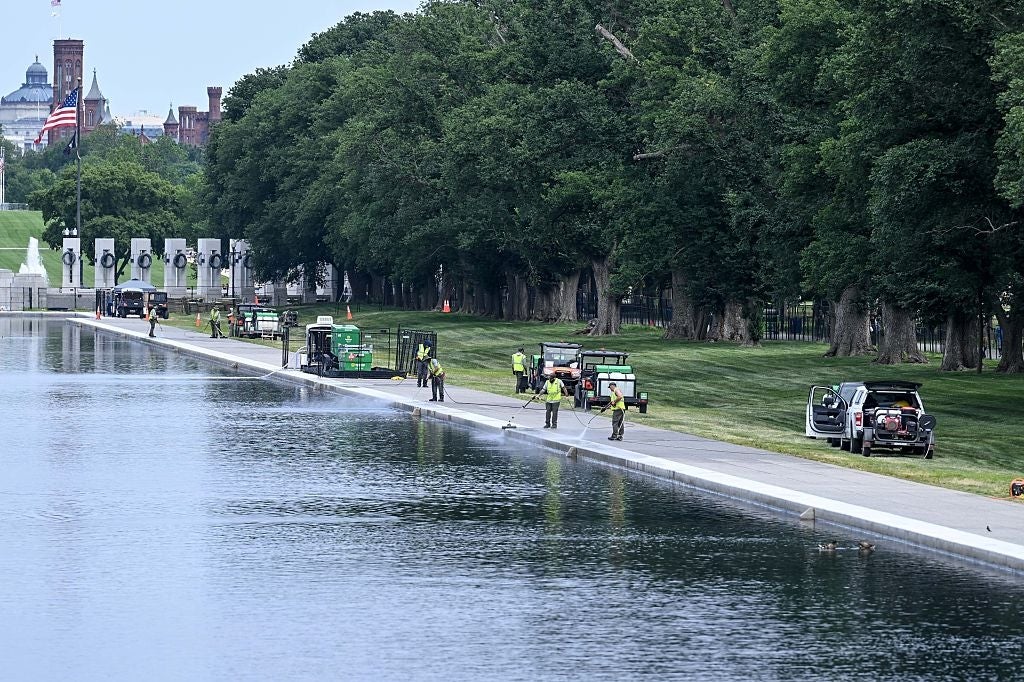 Arbeidere vedlikeholder Reflecting Pool-området i Washington, DC, med utstyr rundt seg. Trær og bygninger er synlige i bakgrunnen