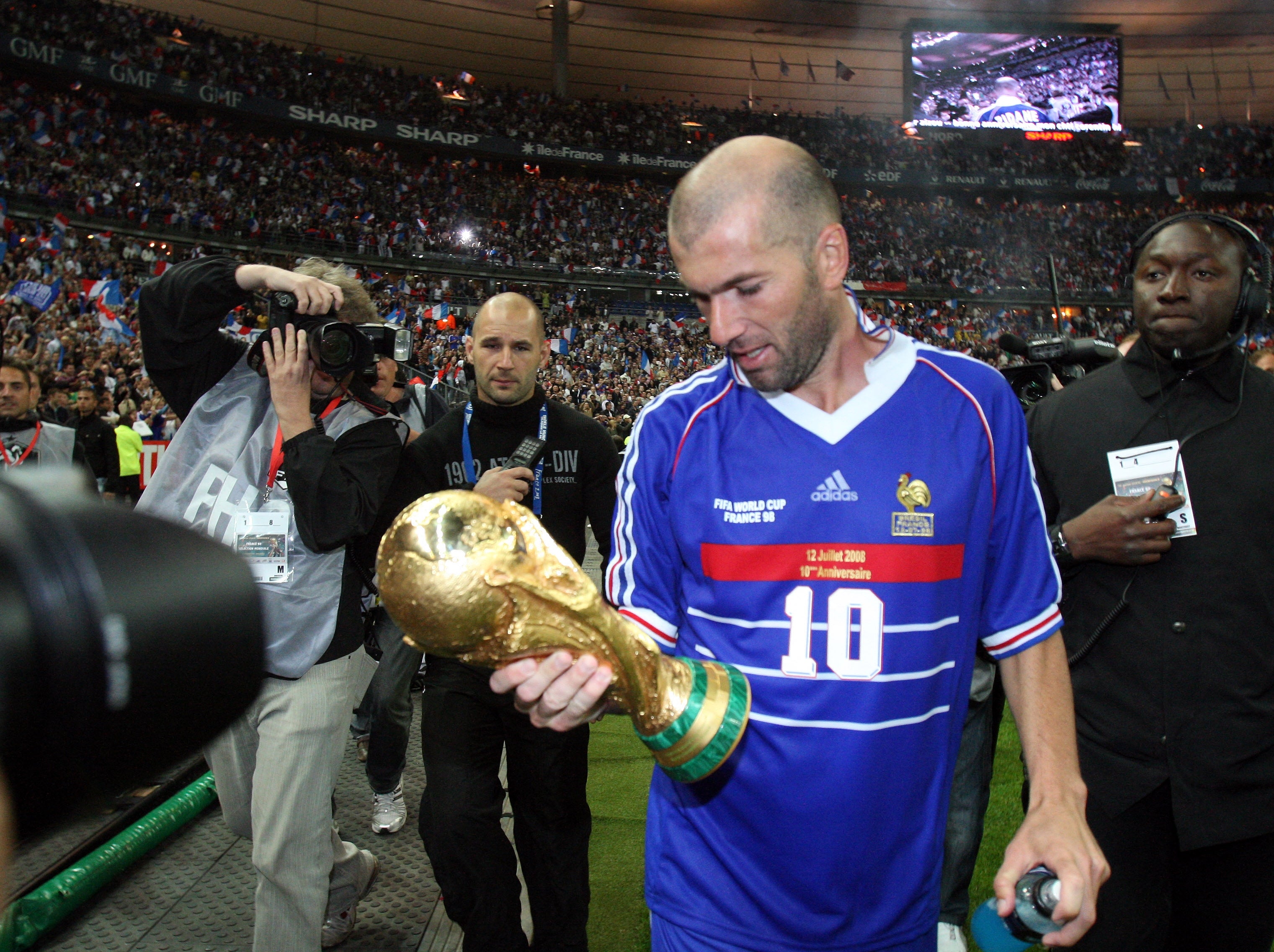 Soccer subordinate successful jersey with "10" holds FIFA World Cup trophy, surrounded by assemblage and photographers successful a stadium