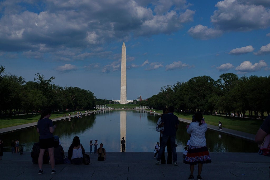 Folk ved Reflecting Pool med Washington-monumentet i det fjerne, under en delvis overskyet himmel