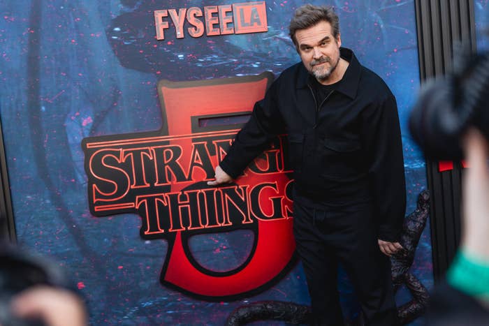 Person successful  achromatic  suit   poses adjacent  to "Stranger Things" motion   astatine  a media event