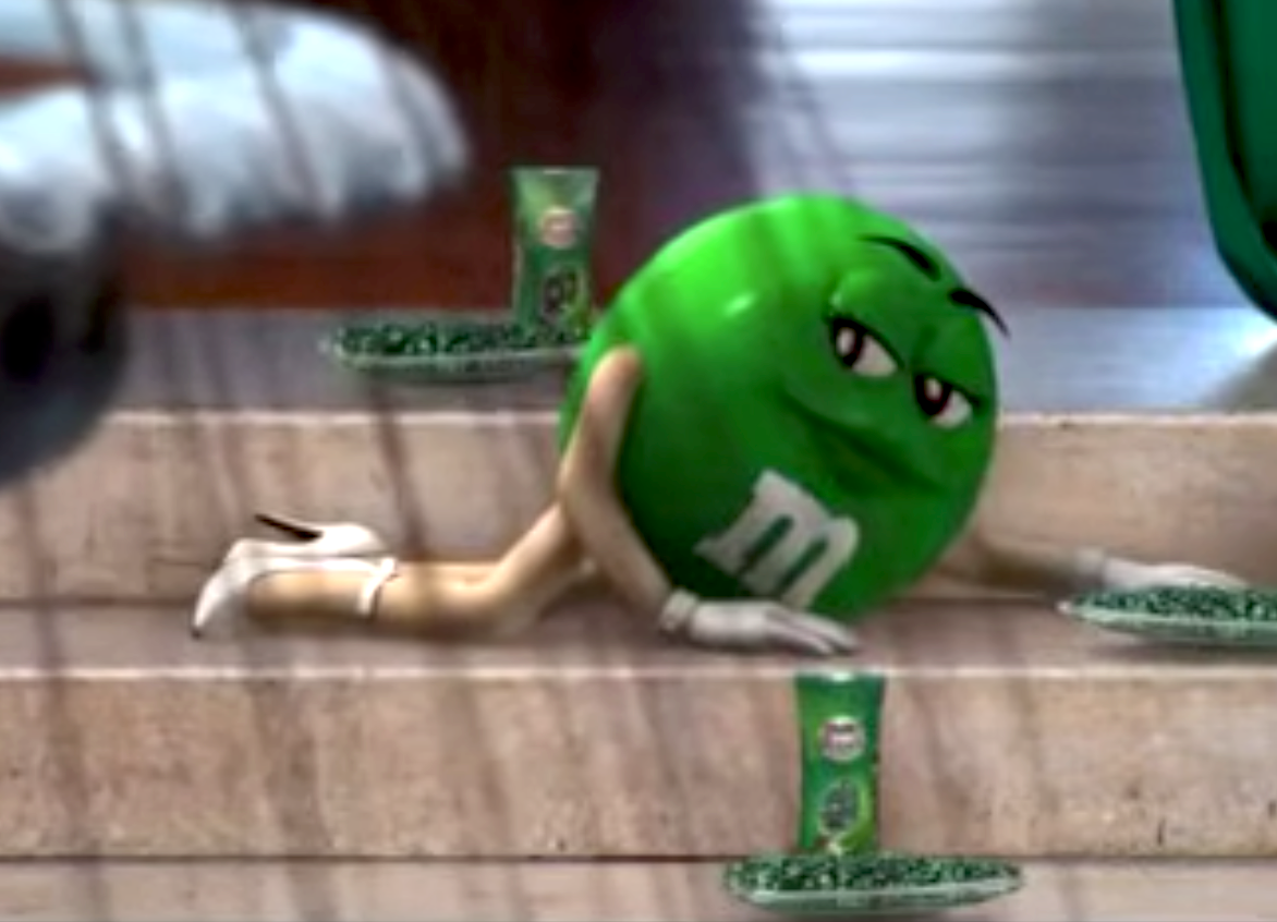 Green M&amp;amp;M quality  lying connected  stairs with a sly expression, surrounded by greenish  candy bags