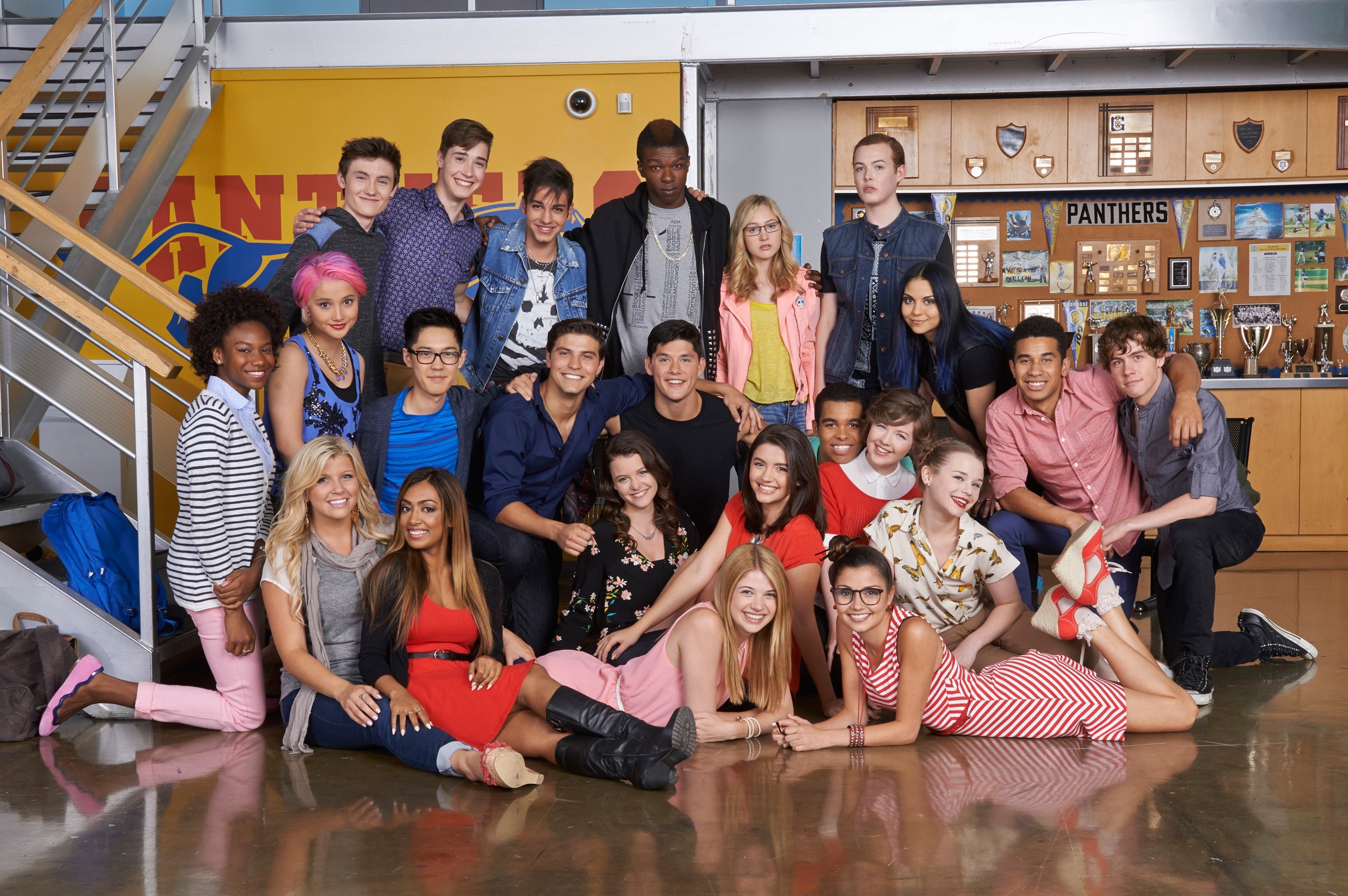 A group of young actors casually pose together indoors, dressed in a variety of casual outfits