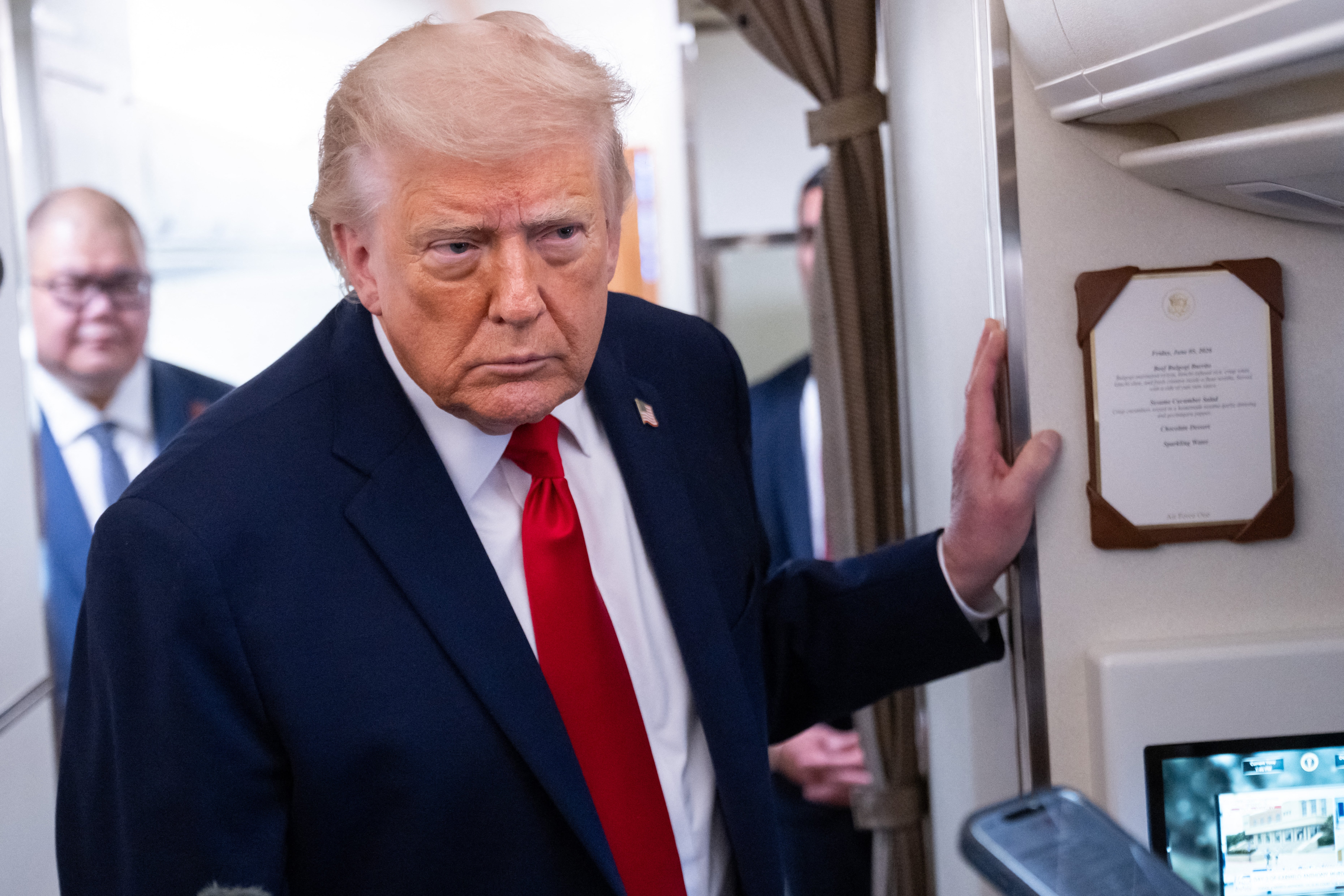 A antheral successful a suit with a reddish necktie is connected an aircraft, lasting adjacent a plaque and holding a handrail. Another idiosyncratic is disposable successful the background