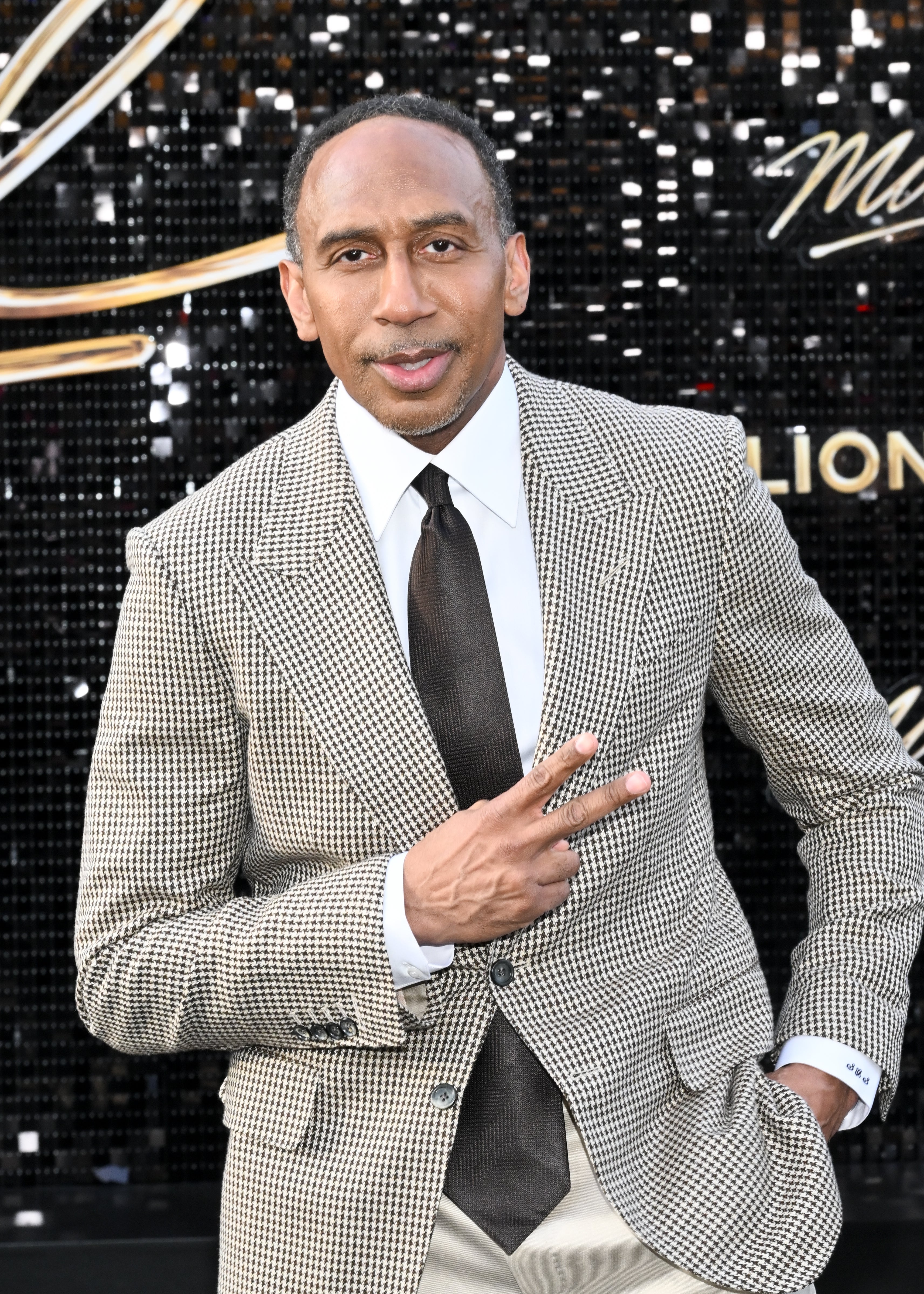 Man successful checkered suit with necktie gives a bid sign, lasting successful beforehand of a sparkling backdrop
