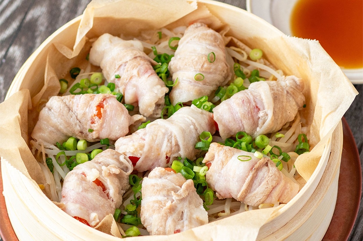蒸し器に盛られた豚肉の野菜巻き料理。小口切りねぎがトッピング。横に小皿のタレ。
