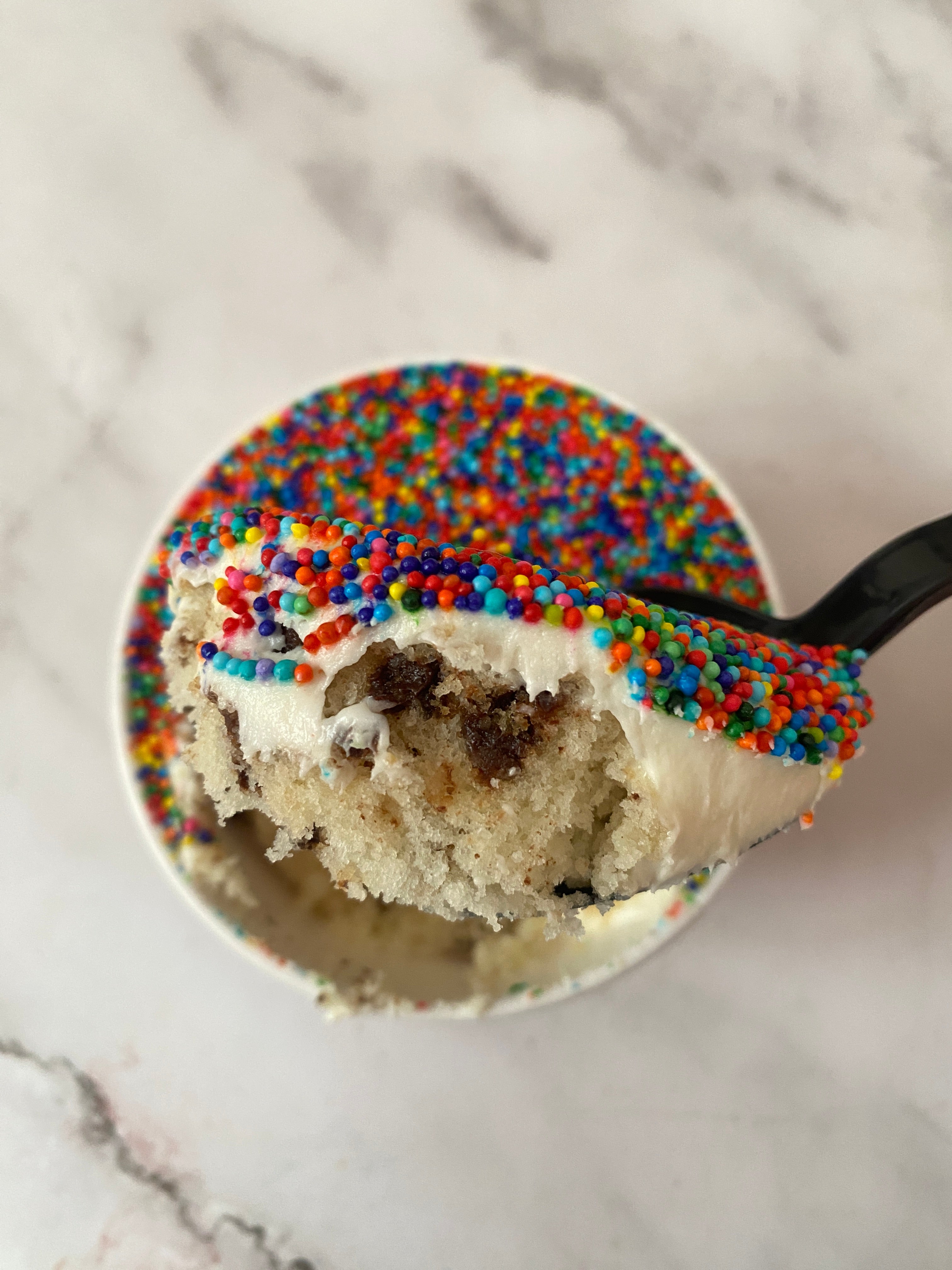Spoon holding a piece of cake topped with colorful sprinkles, against a background of more cake