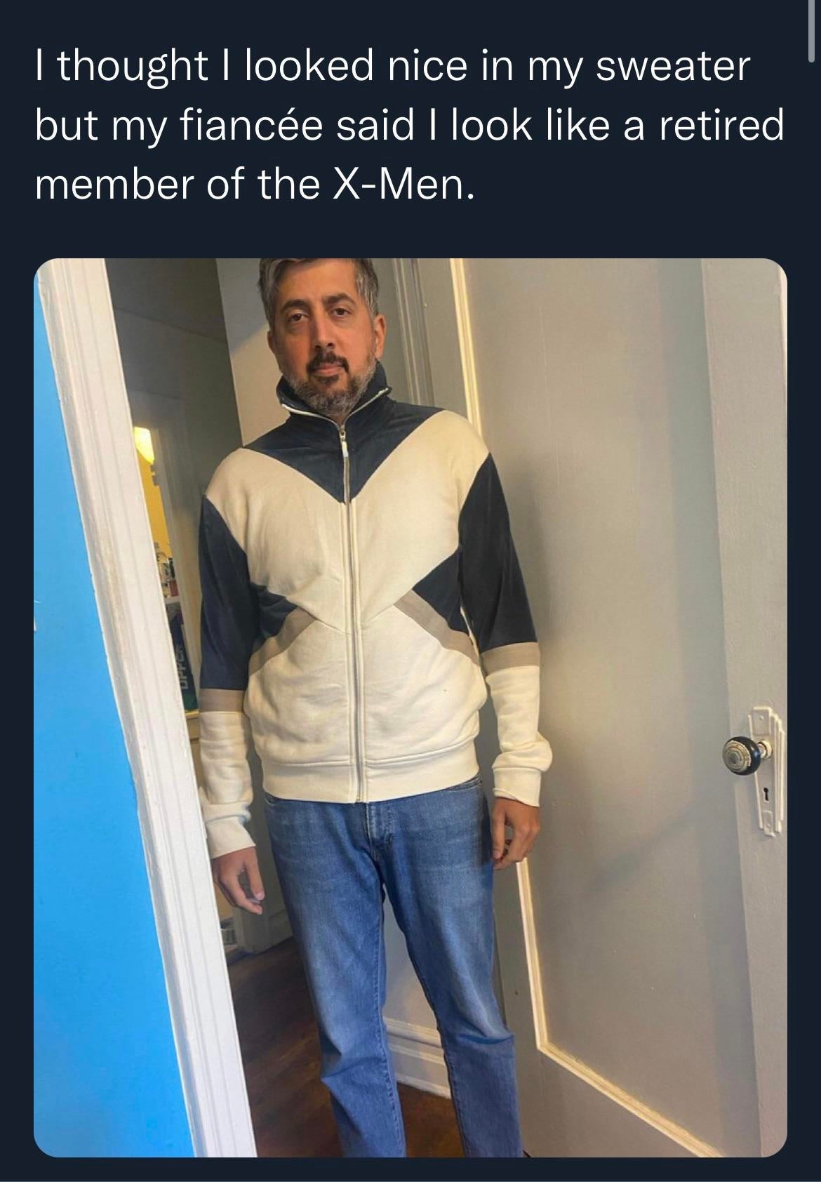 Man successful  geometric-patterned sweater, resembling superhero attire, stands humorously successful  a hallway, reacting to fiancée's remark  astir  his look