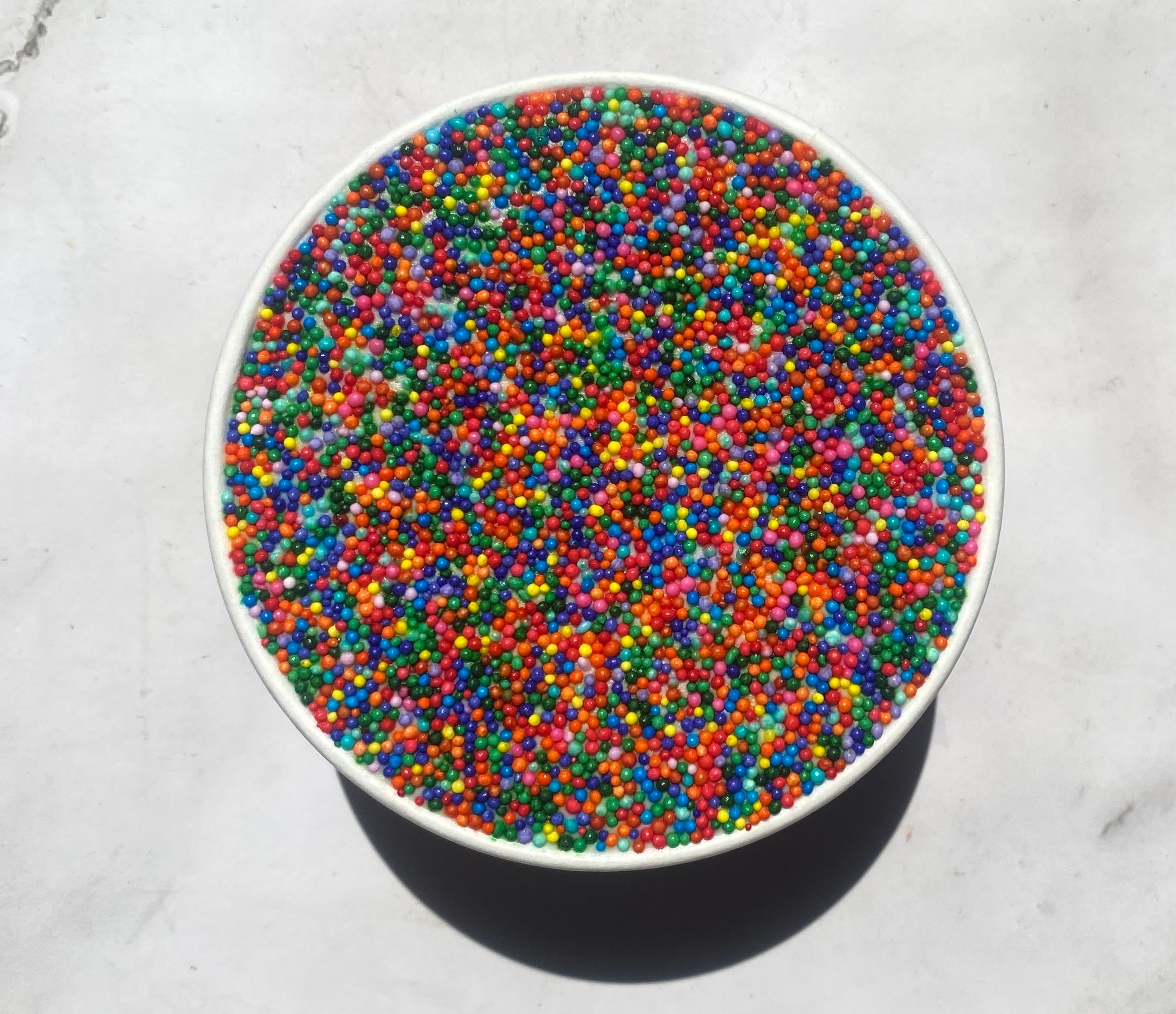 Bowl filled with multicolored candy sprinkles, placed on a light surface