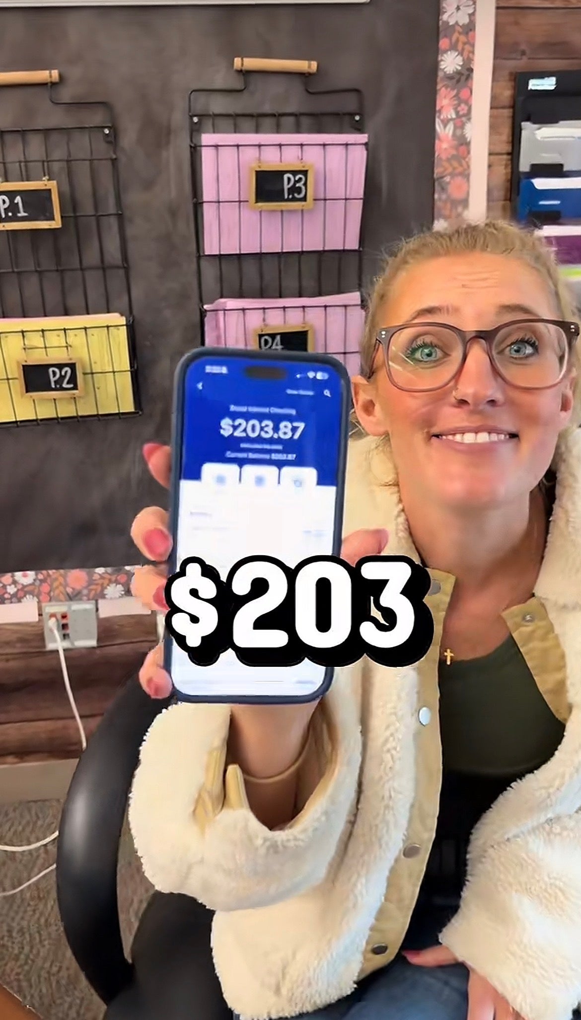 Person smiling and holding up   a telephone  displaying an app with a equilibrium  of $203.87