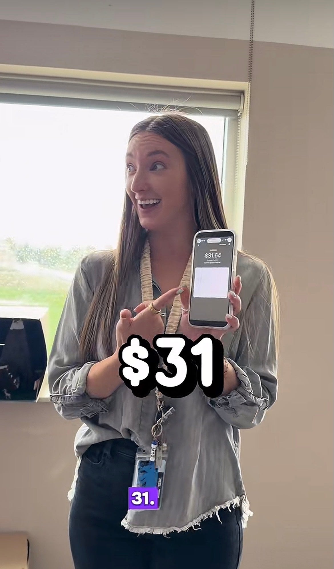 Person holding a telephone  with "$31" disposable   connected  the screen, smiling, wearing a casual blouse and lanyard successful  an indoor setting