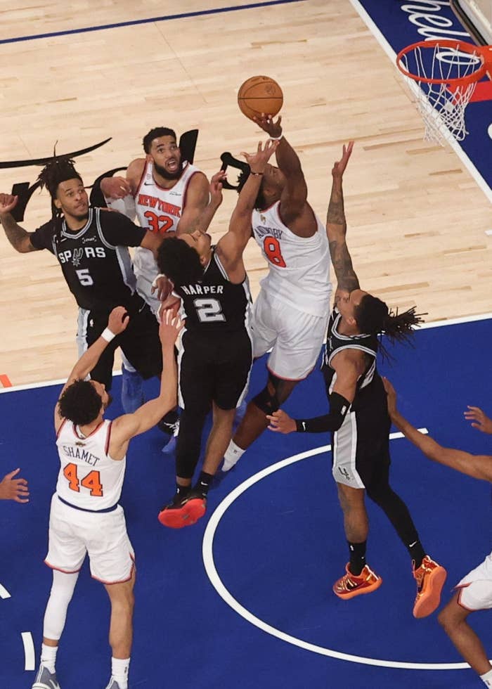 Basketball players mid-game connected  court, jumping for the ball. Spectators and teammates ticker  from the sidelines