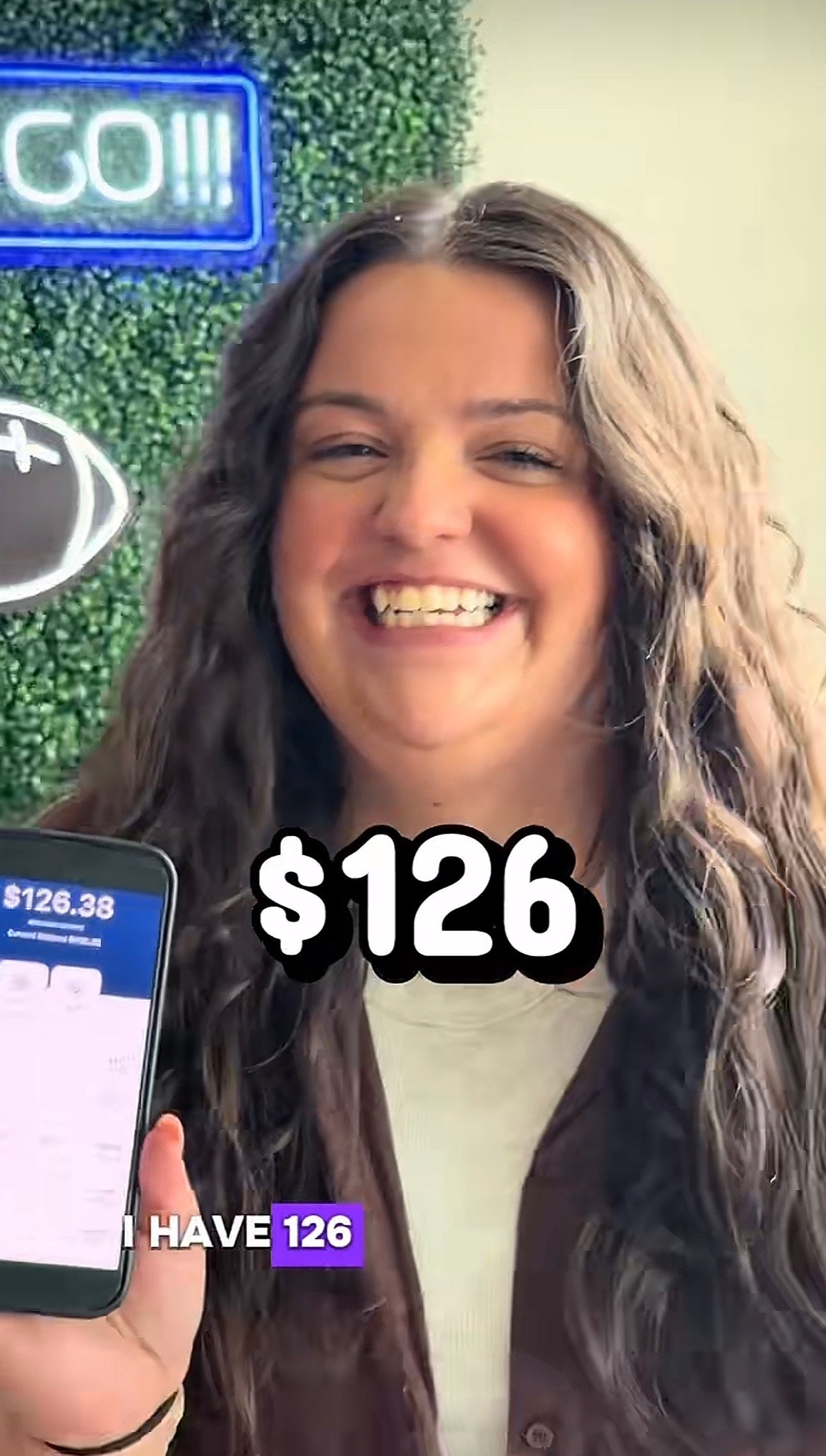 Smiling idiosyncratic   holding a telephone  displaying a $126 net  app screen