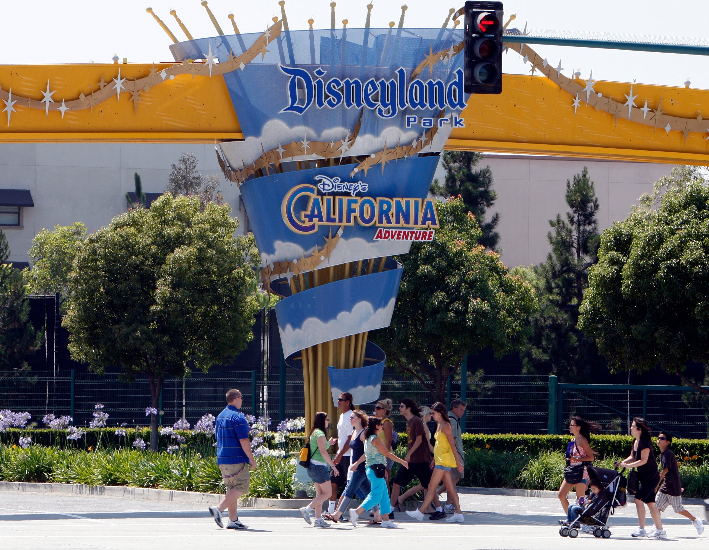 People walking nether a Disneyland Park motion with a Disney California Adventure logo, surrounded by trees and flowers