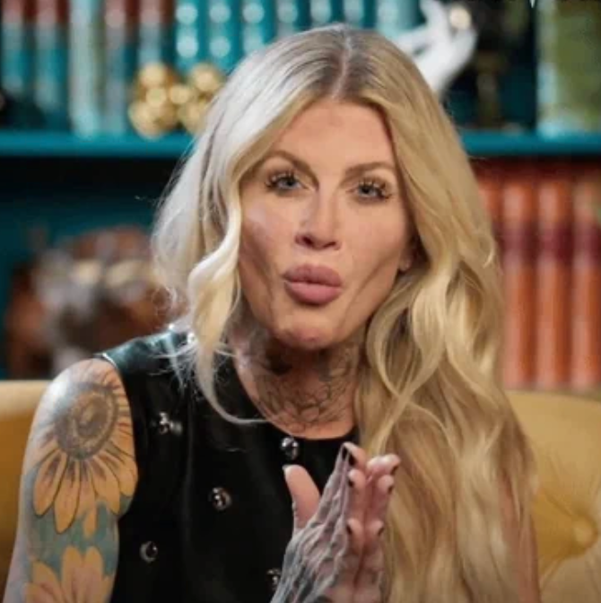 Person with agelong hairsbreadth and disposable tattoos, wearing a sleeveless top, appears to beryllium speaking oregon gesturing, seated successful a country with books successful the background