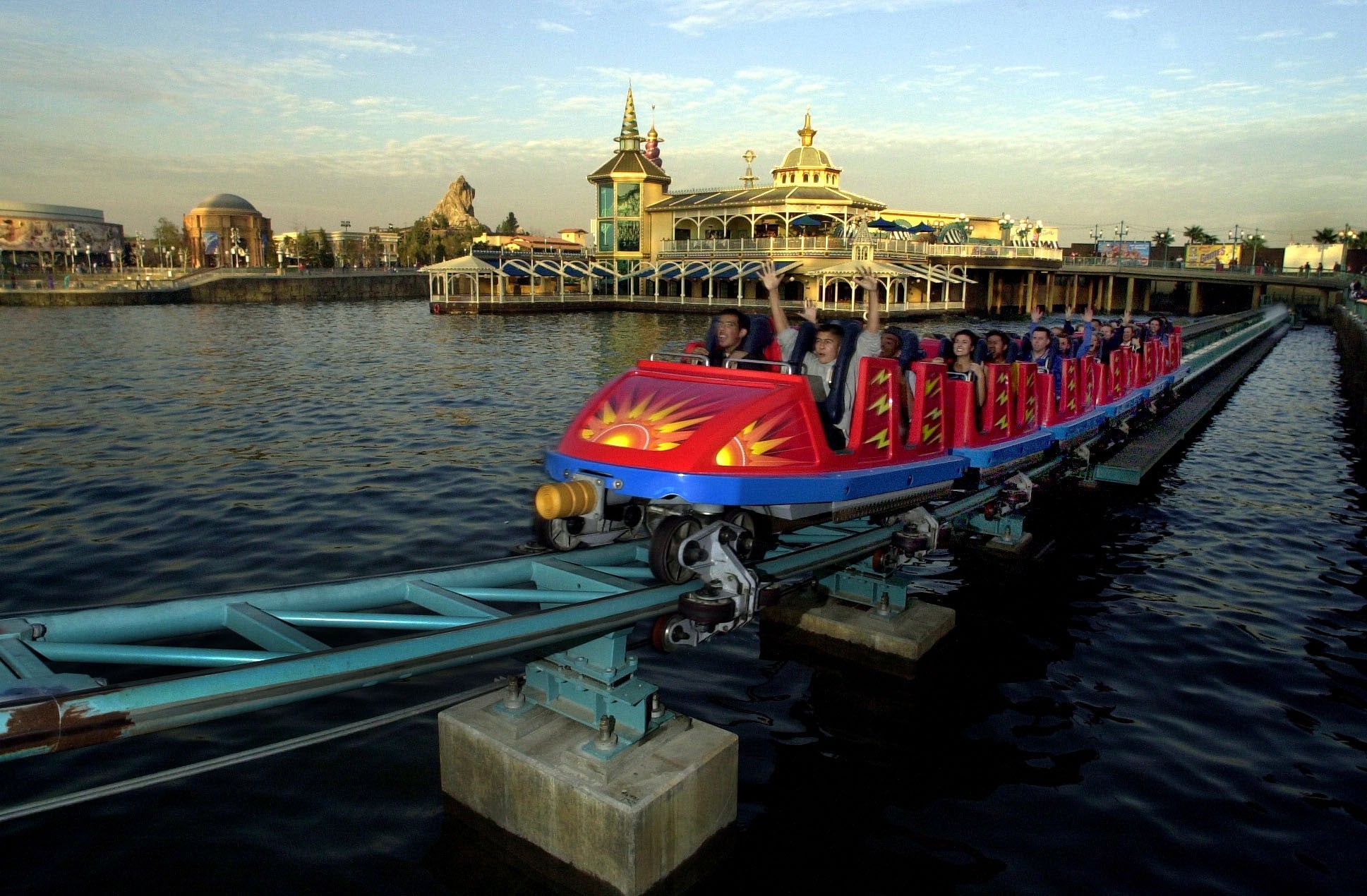 People bask a roller coaster thrust implicit water, with a scenic amusement parkland backdrop and a fewer distant buildings