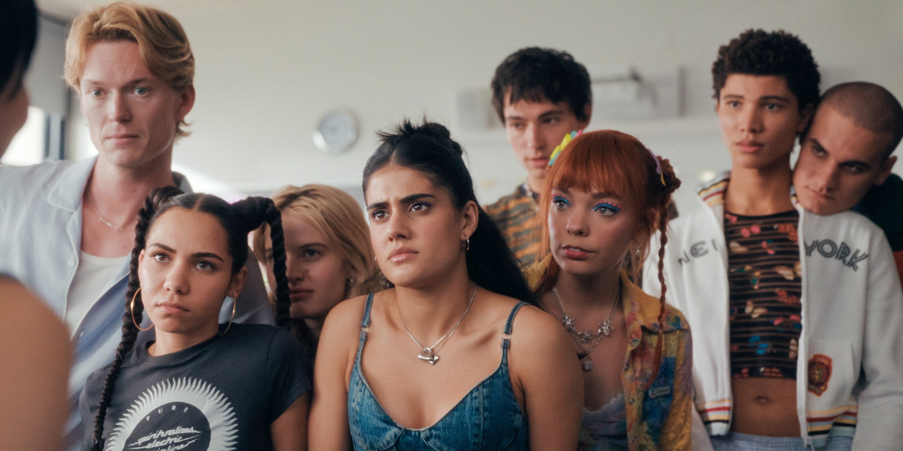 A group of serious young adults in casual, contemporary outfits gather closely, appearing engaged in a conversation or scene