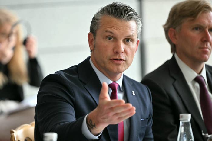 A idiosyncratic   successful  a suit   gestures portion    speaking astatine  a league  table, with different  idiosyncratic  seated nearby, attentively listening