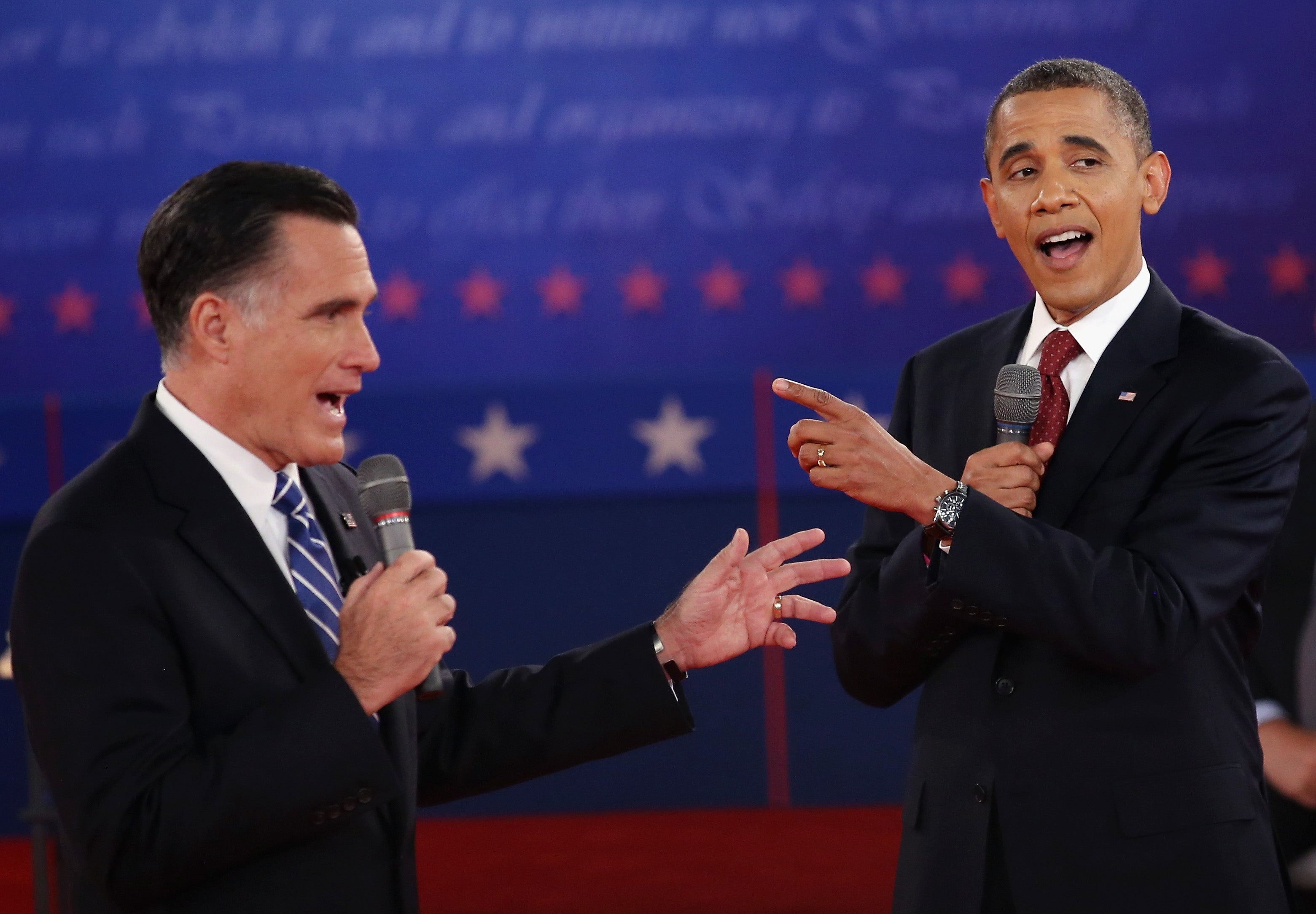 Two men successful suits speaking astatine a debate, gesturing with microphones successful hand, successful beforehand of a backdrop with stars