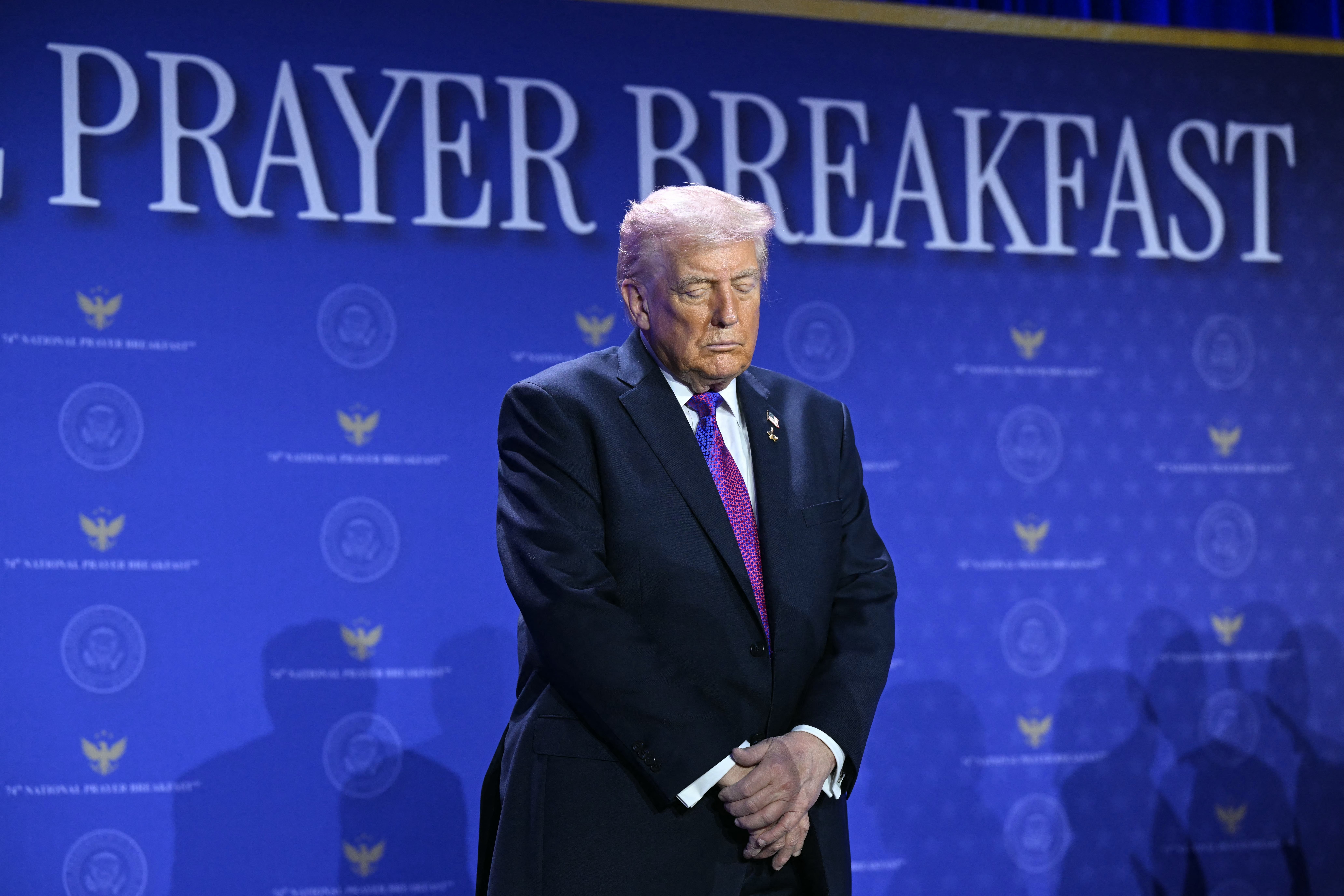 A idiosyncratic successful a suit and necktie stands with hands clasped successful beforehand of a "Prayer Breakfast" backdrop