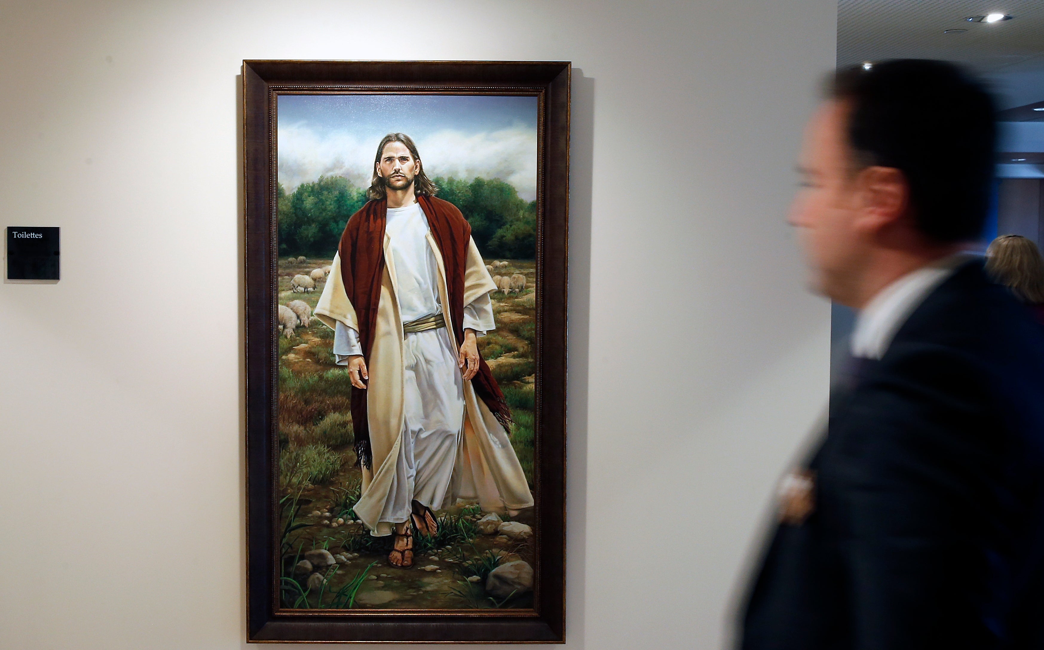 A blurred fig walks past a coating depicting a idiosyncratic successful robes beside rocks and trees, displayed successful an creation gallery