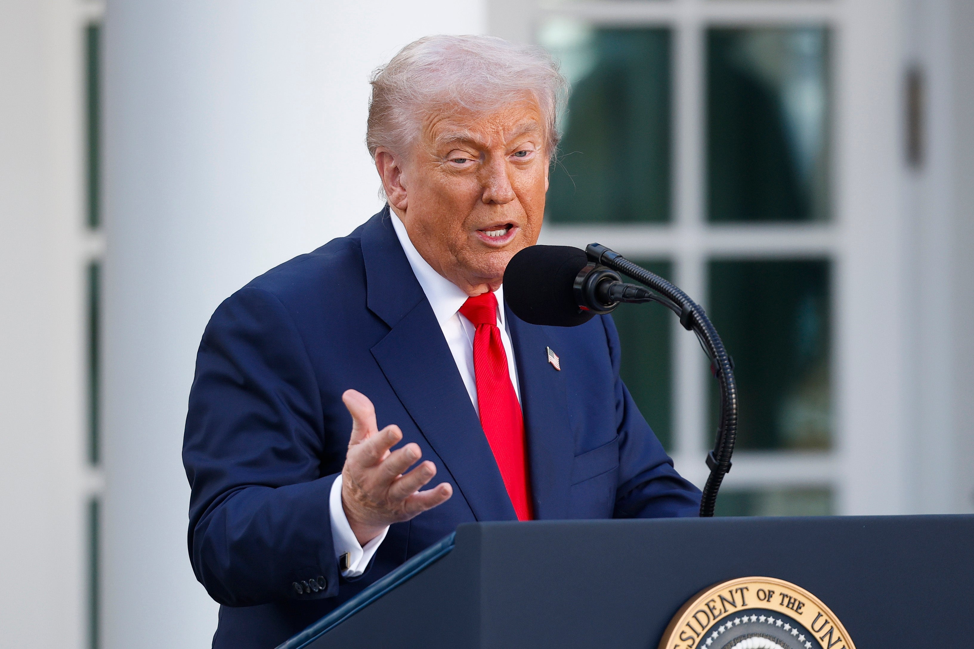 A idiosyncratic successful a suit speaks astatine a podium with a statesmanlike seal, gesturing with 1 manus astatine an outdoor event