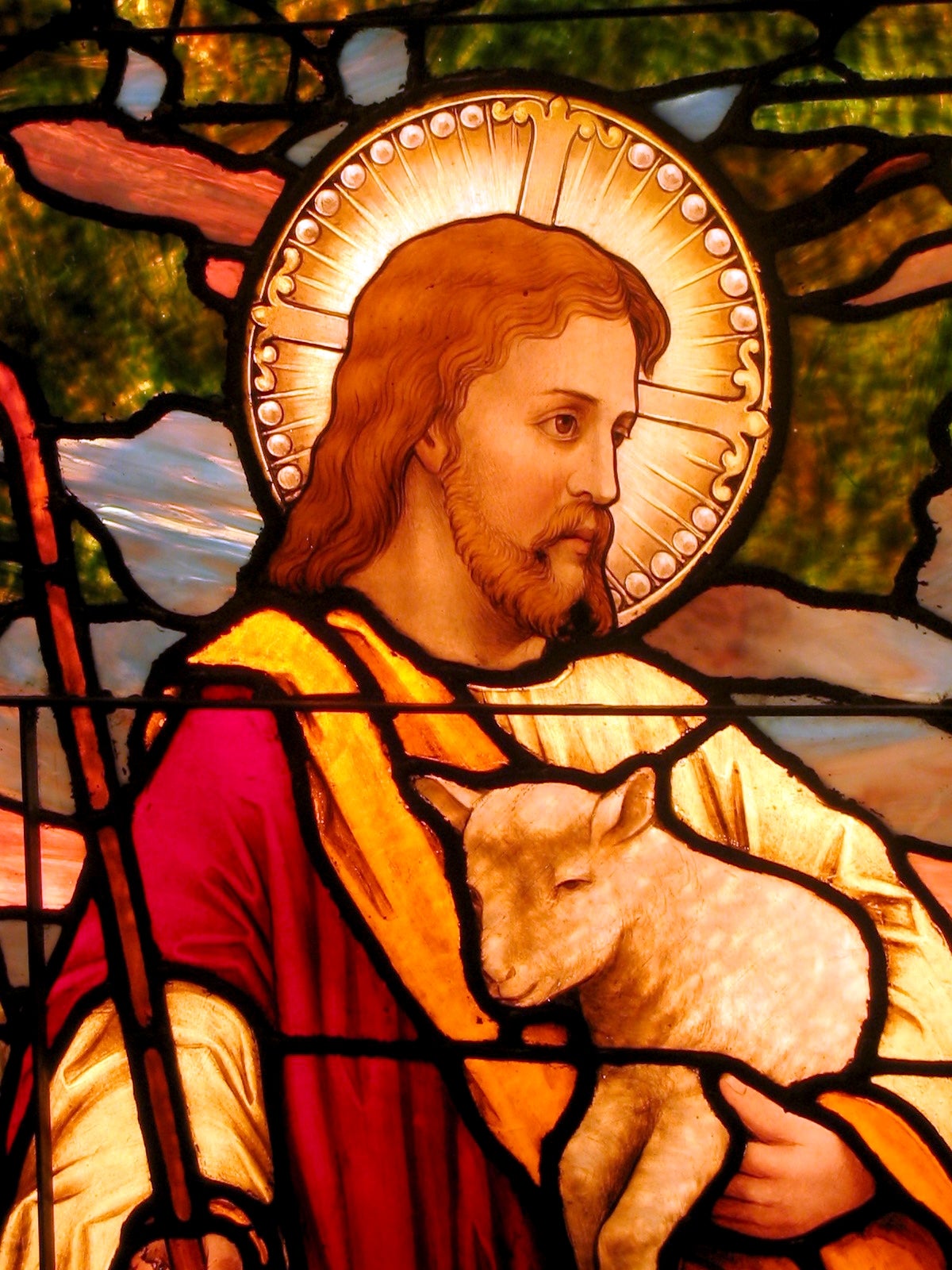 Stained solid depiction of a bearded fig holding a lamb, with a halo supra his head, surrounded by ornate patterns and designs
