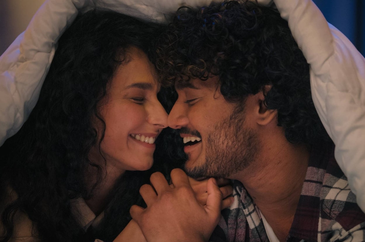 A couple smiling and holding hands under a blanket, enjoying a tender moment