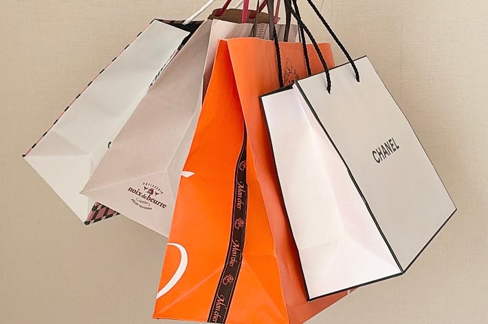 手に持たれた複数のショッピングバッグ。Chanelなどのブランド名が見える。