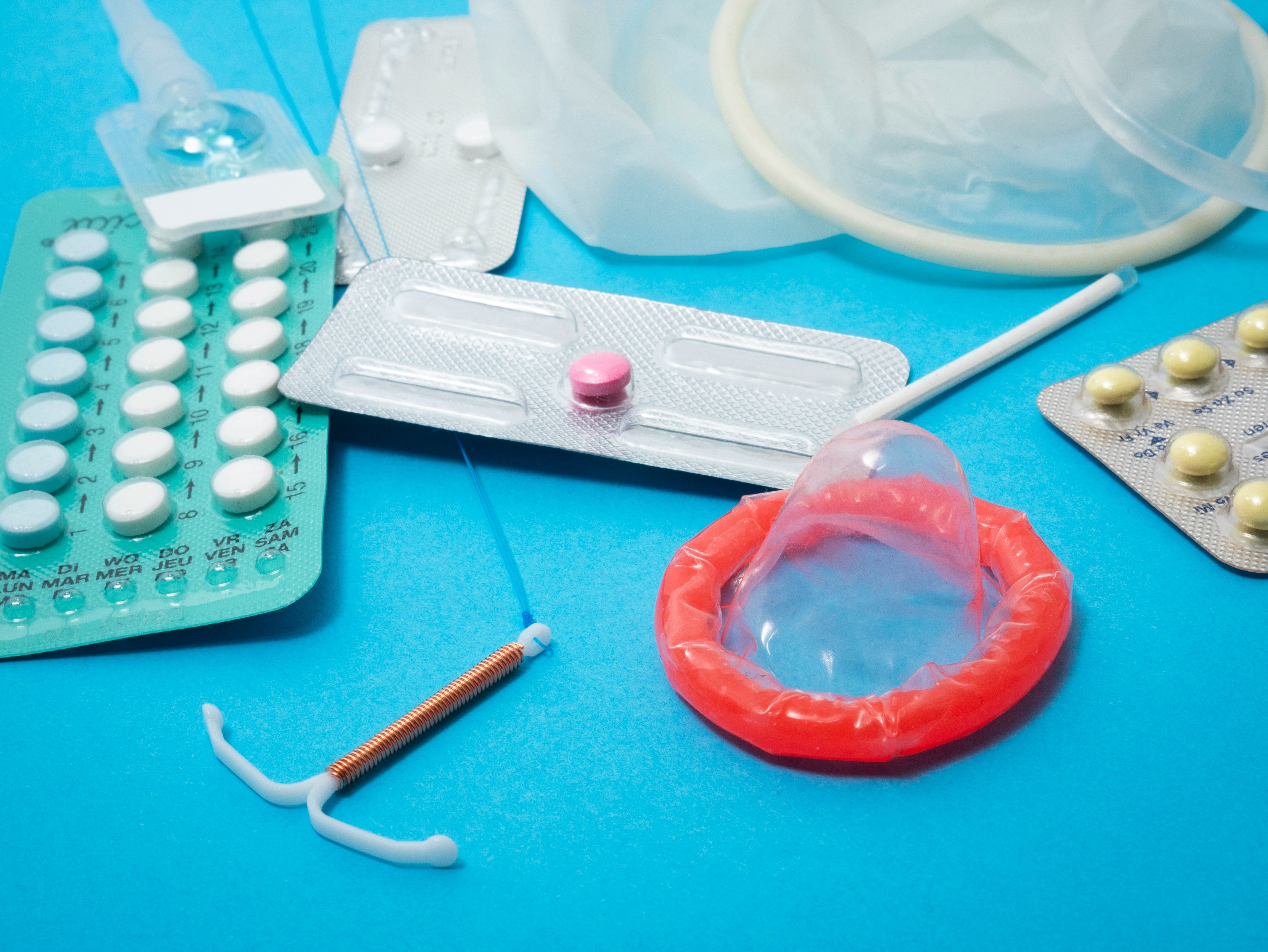 Various contraceptives, including pills, an IUD, a condom, and more, are displayed connected a bluish surface