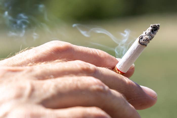 A close-up of a manus  holding a lit cigaret  with fume  drifting upward