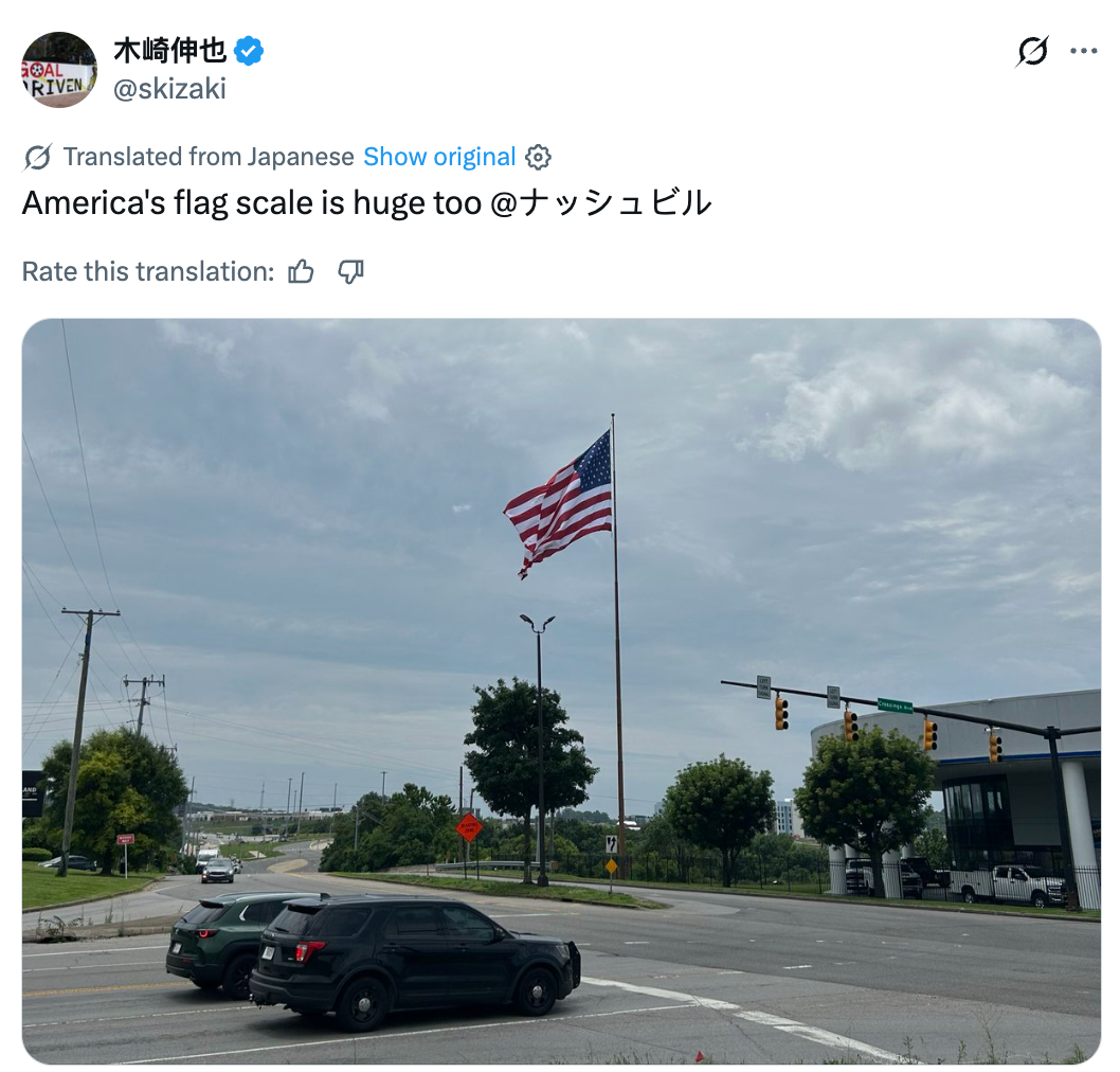 A ample  American emblem  connected  a rod  adjacent   an intersection with cars and trees visible, highlighted successful  a societal  media station  translation