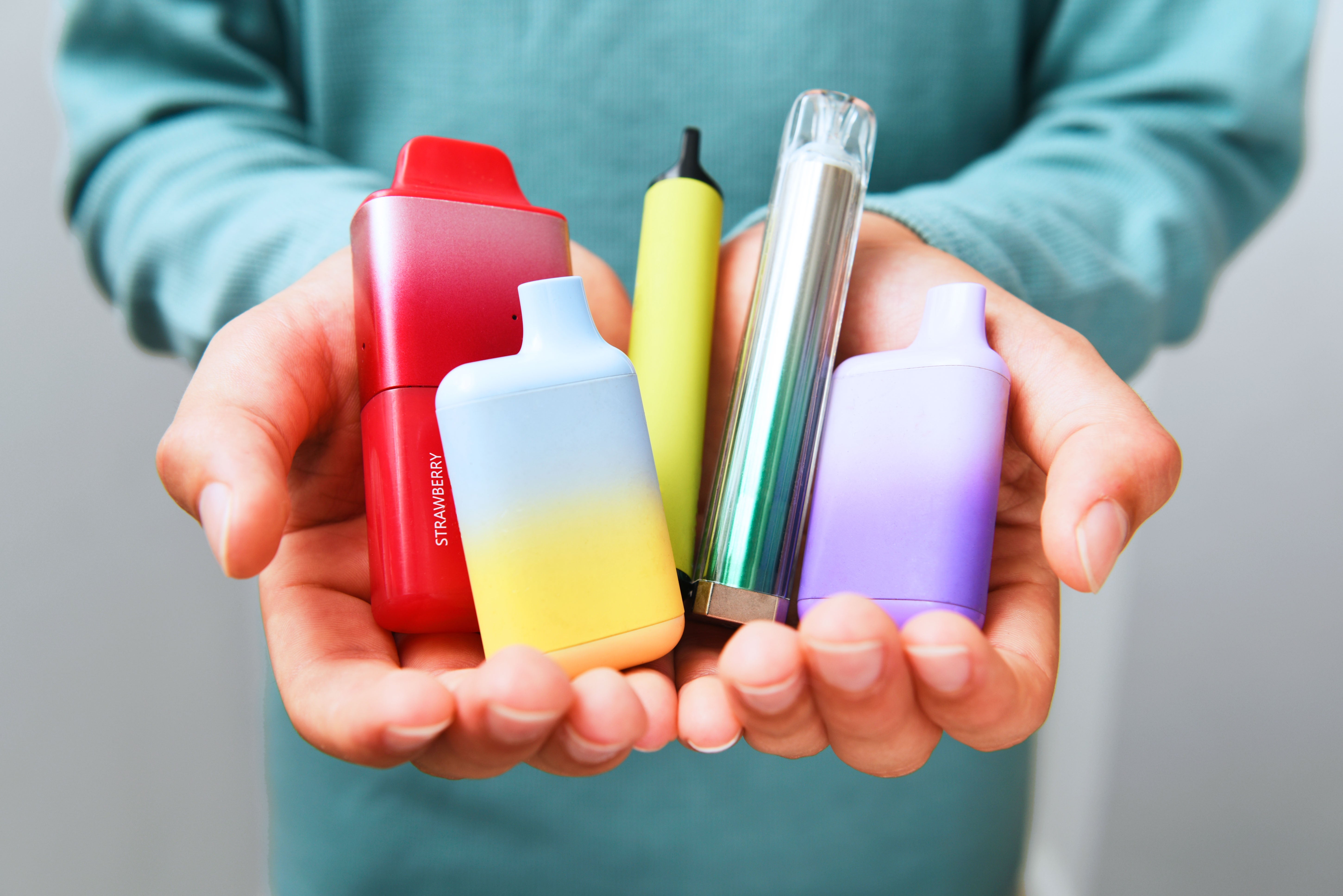Hands holding assorted colorful vape devices