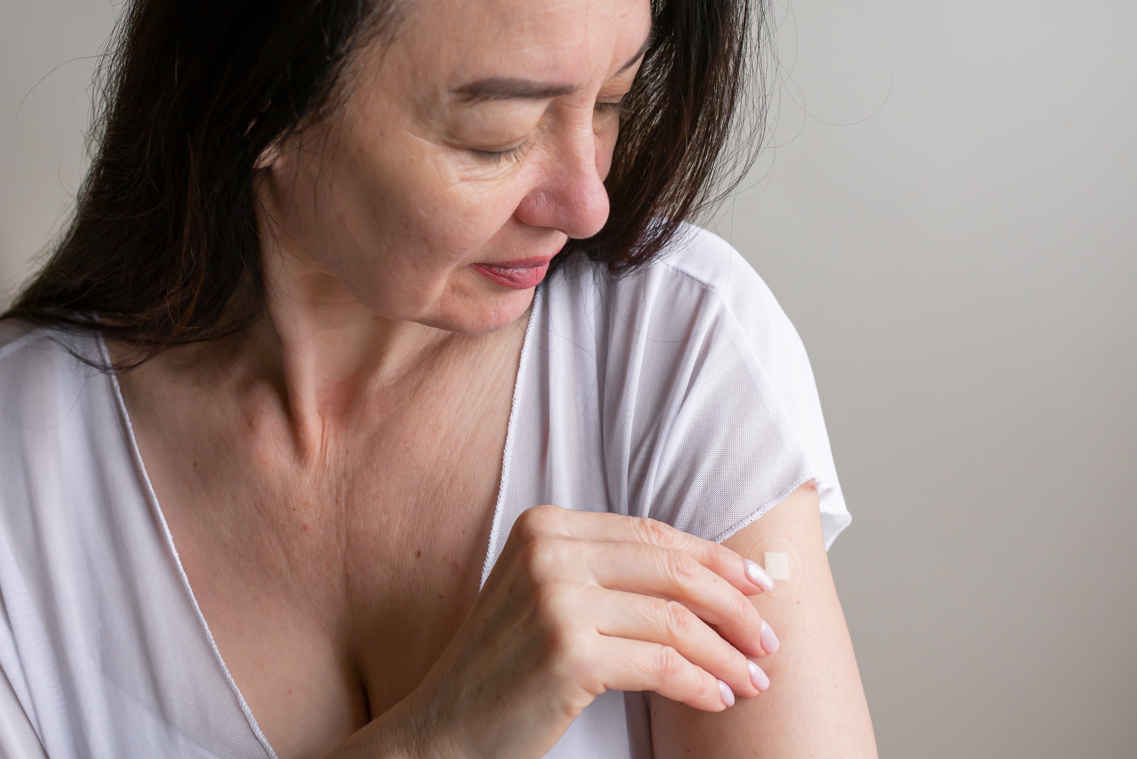 Person successful a achromatic garment looks astatine a bandage connected their arm, suggesting post-vaccination care