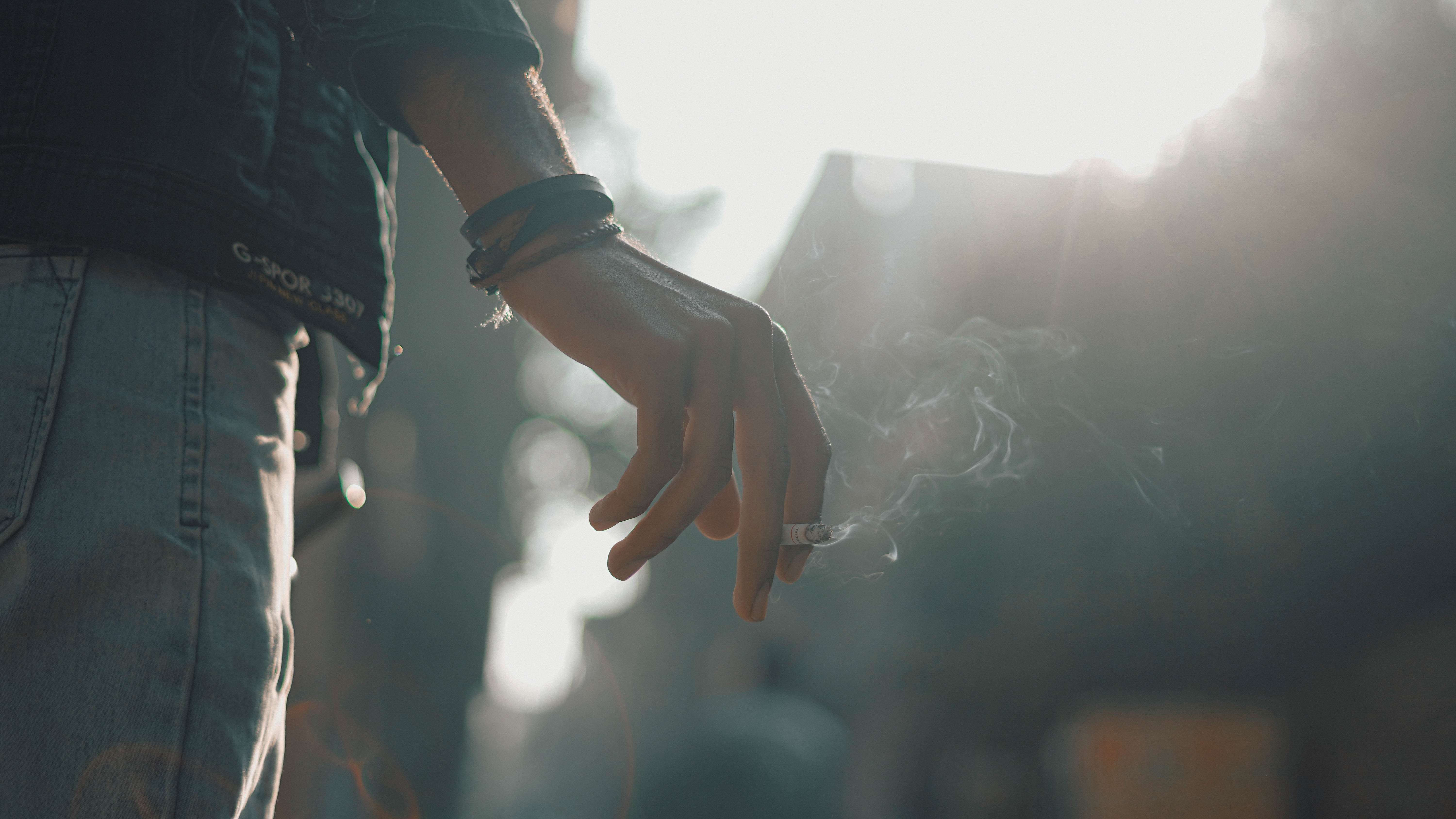 Person holding a cigarette, casually lasting outdoors with fume visible