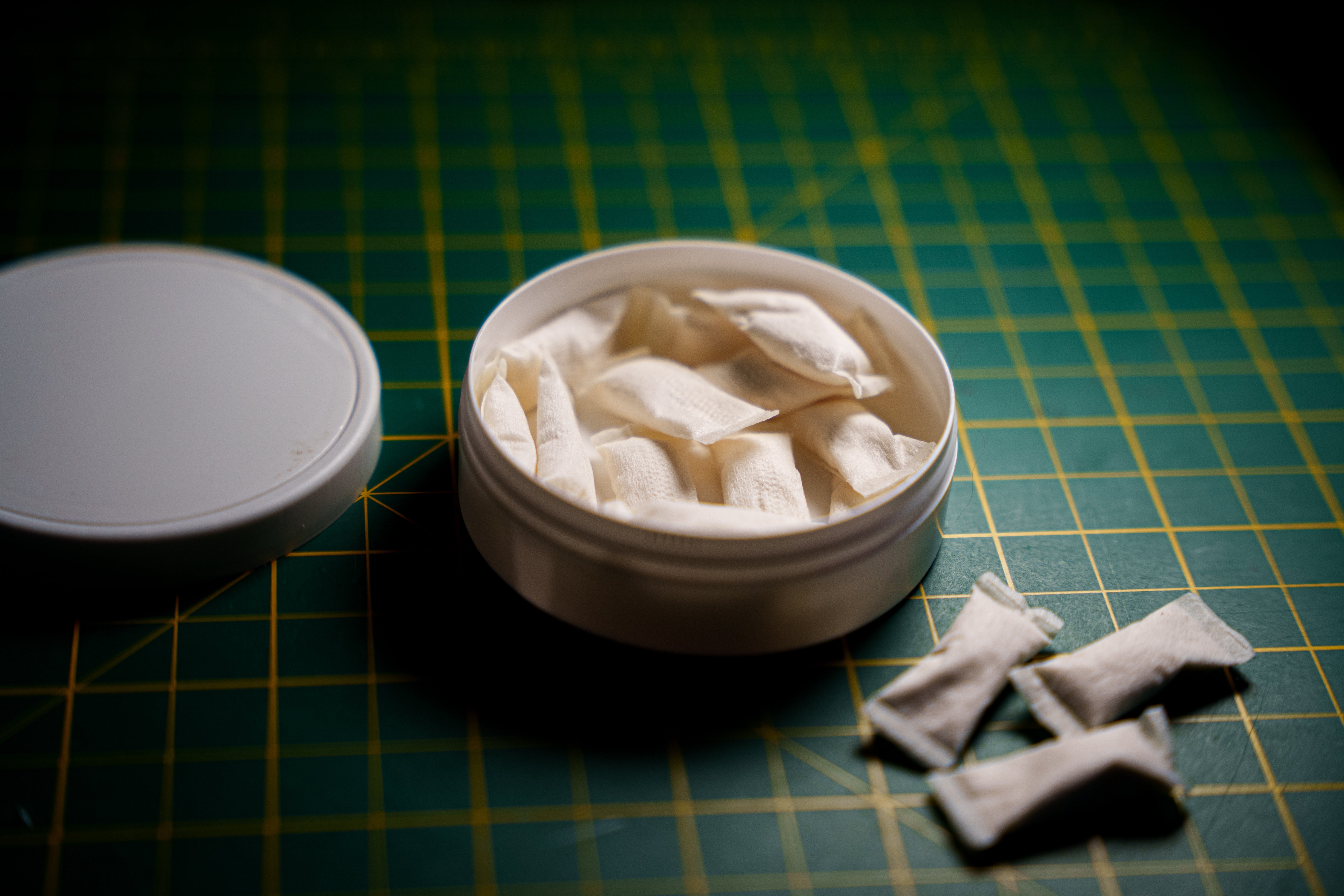 Open achromatic instrumentality of nicotine pouches connected a grid surface, with a fewer pouches beside the container