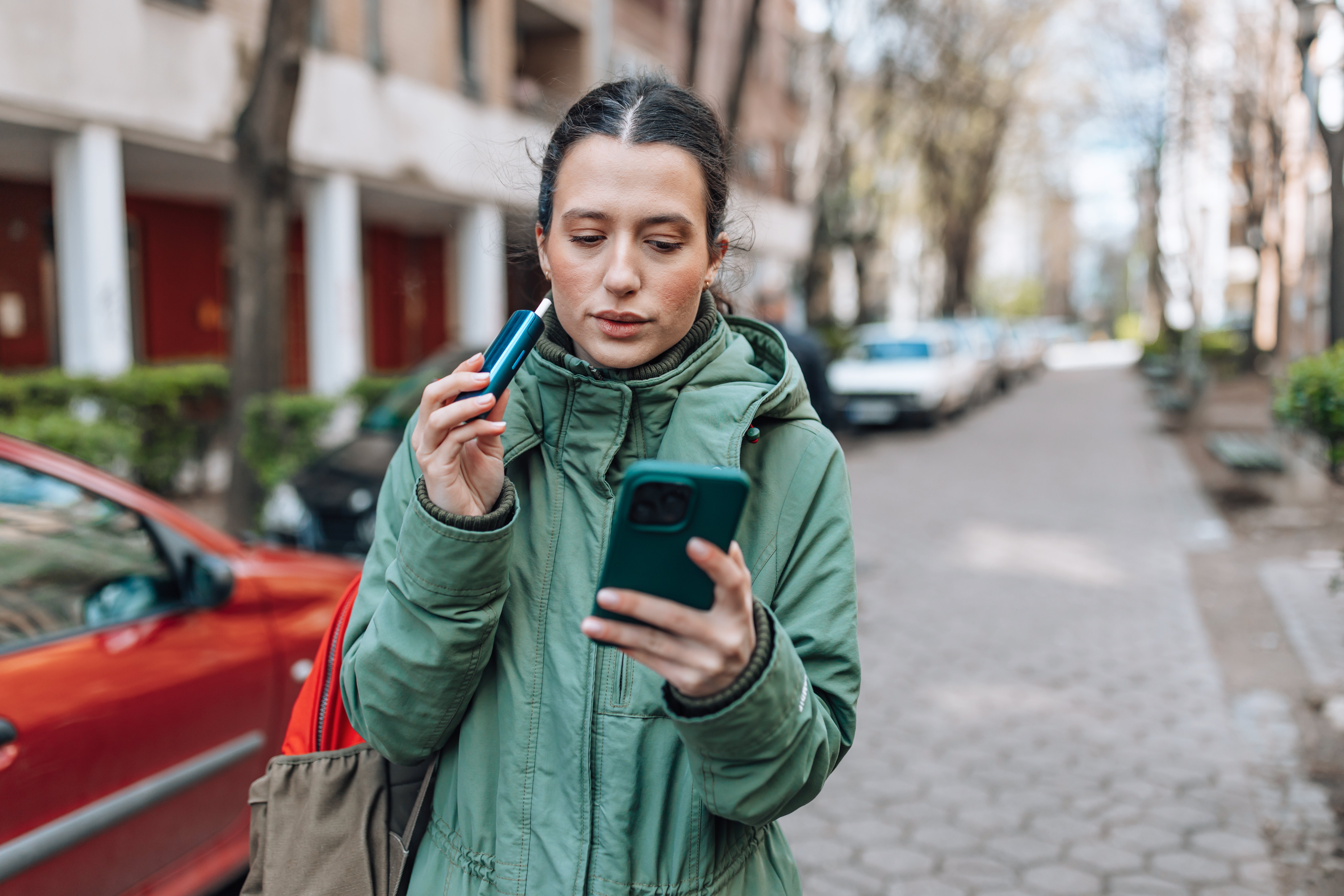 Person utilizing an inhaler portion checking telephone outdoors, wearing a lukewarm coat, suggesting wellness absorption oregon allergy prevention