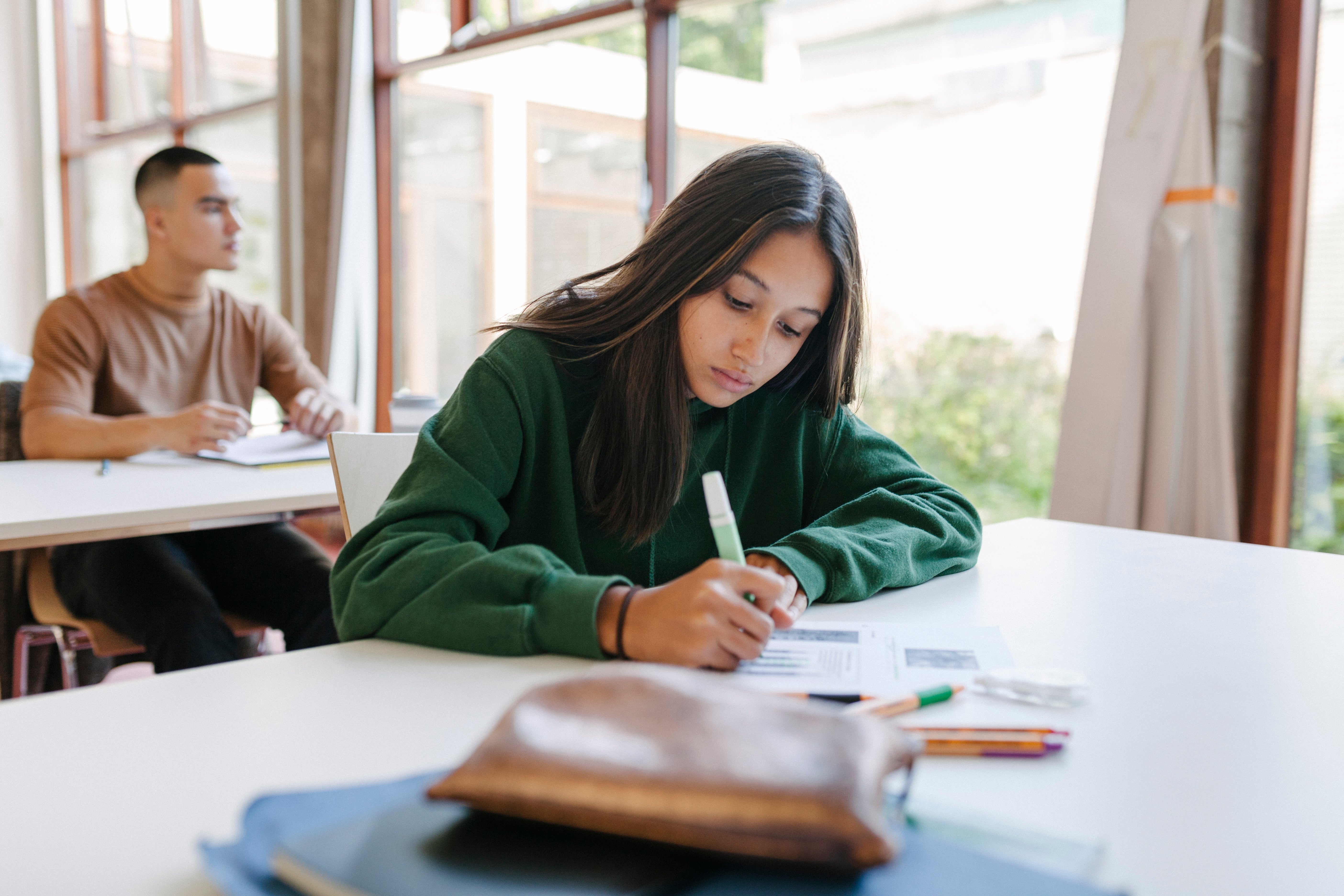Student successful a schoolroom penning successful a notebook, with different pupil successful the inheritance moving astatine a desk