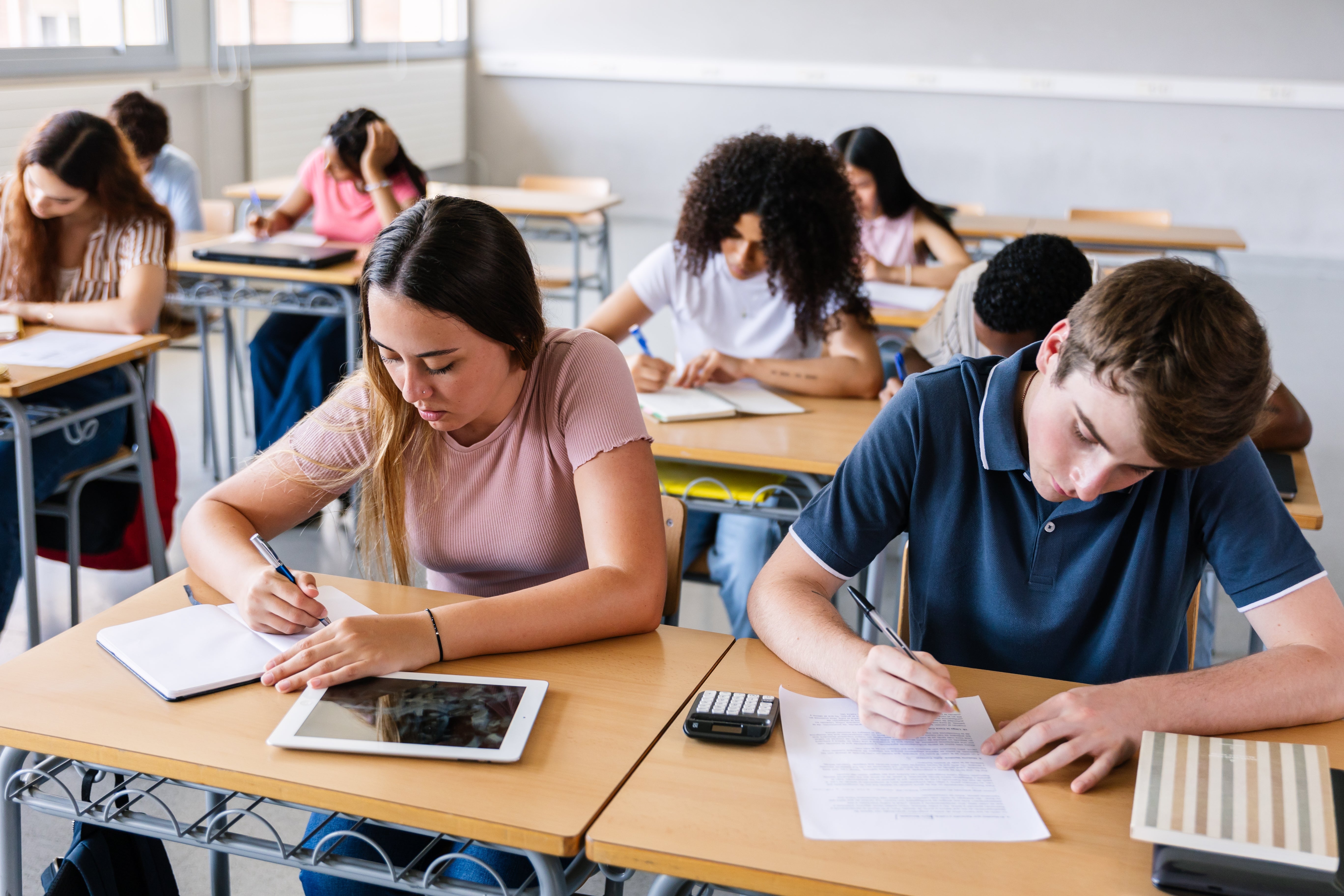 Students seated successful a schoolroom absorption intently connected taking a written exam, each with papers and calculators connected their desks