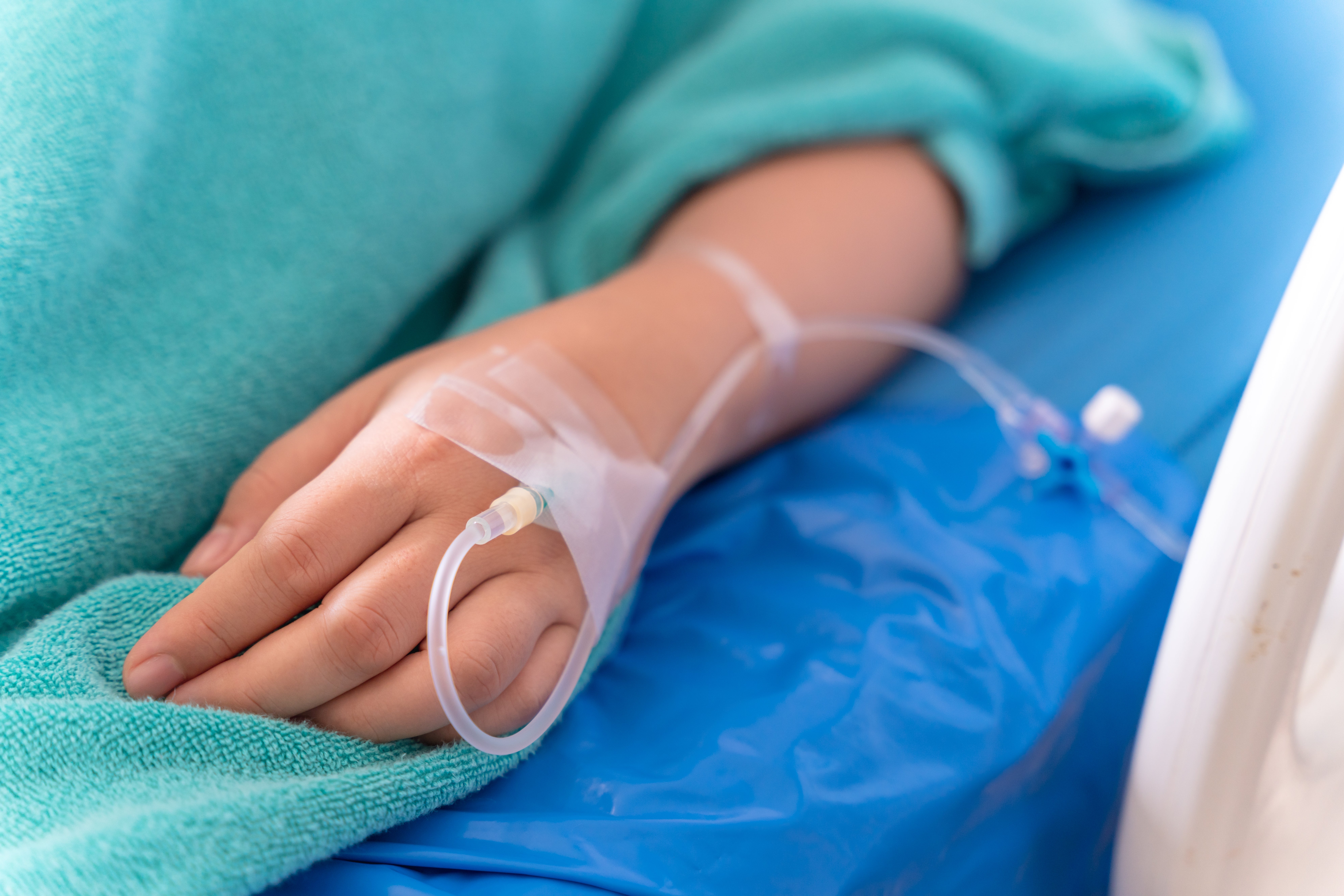 A person's manus is seen with an IV drip inserted, resting connected a infirmary bed