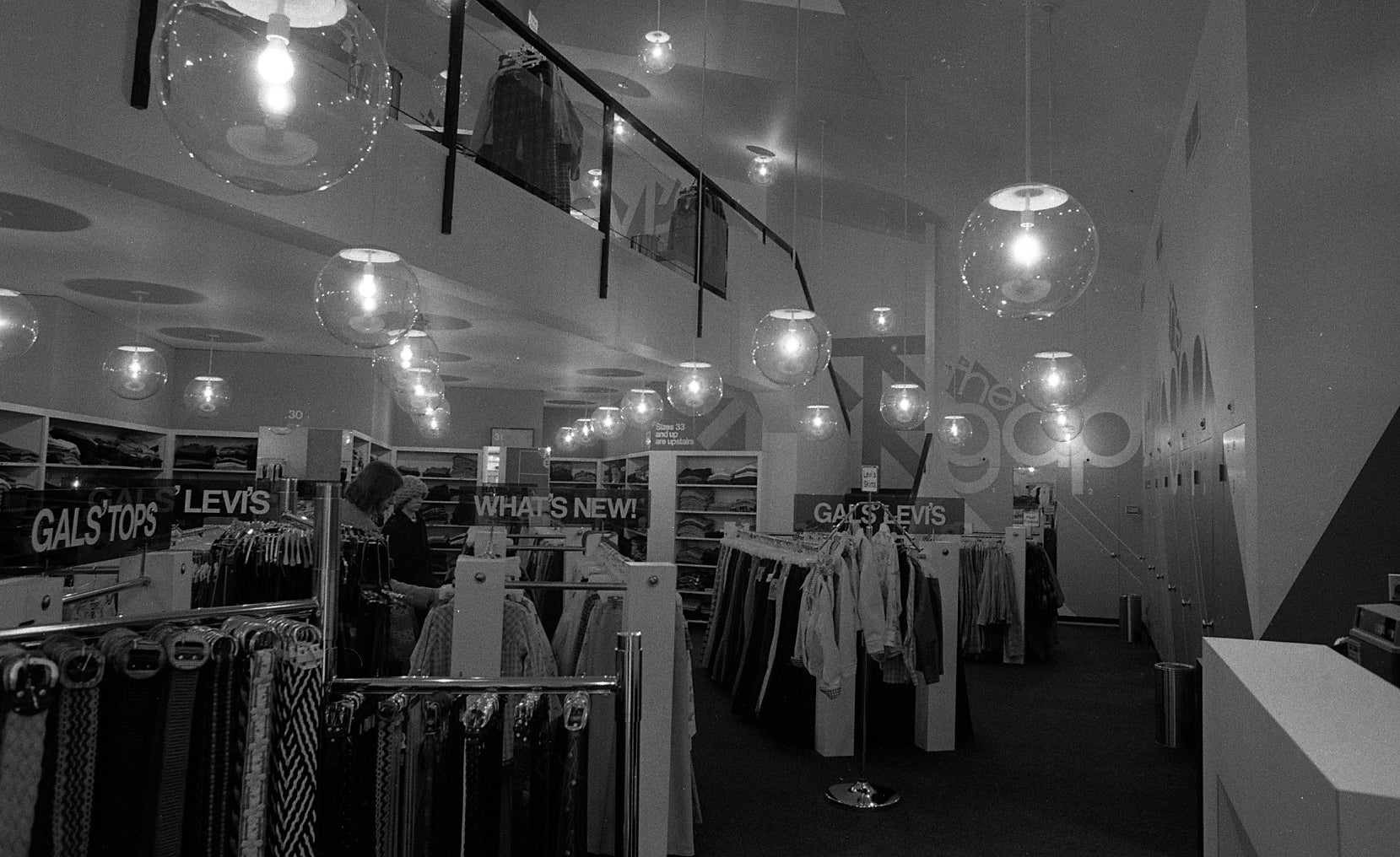 Vintage covering  store   interior with racks of jeans and signs speechmaking  "Gal's Tops" and "Levi's." Hanging globe lights adhd  to the retro aesthetic