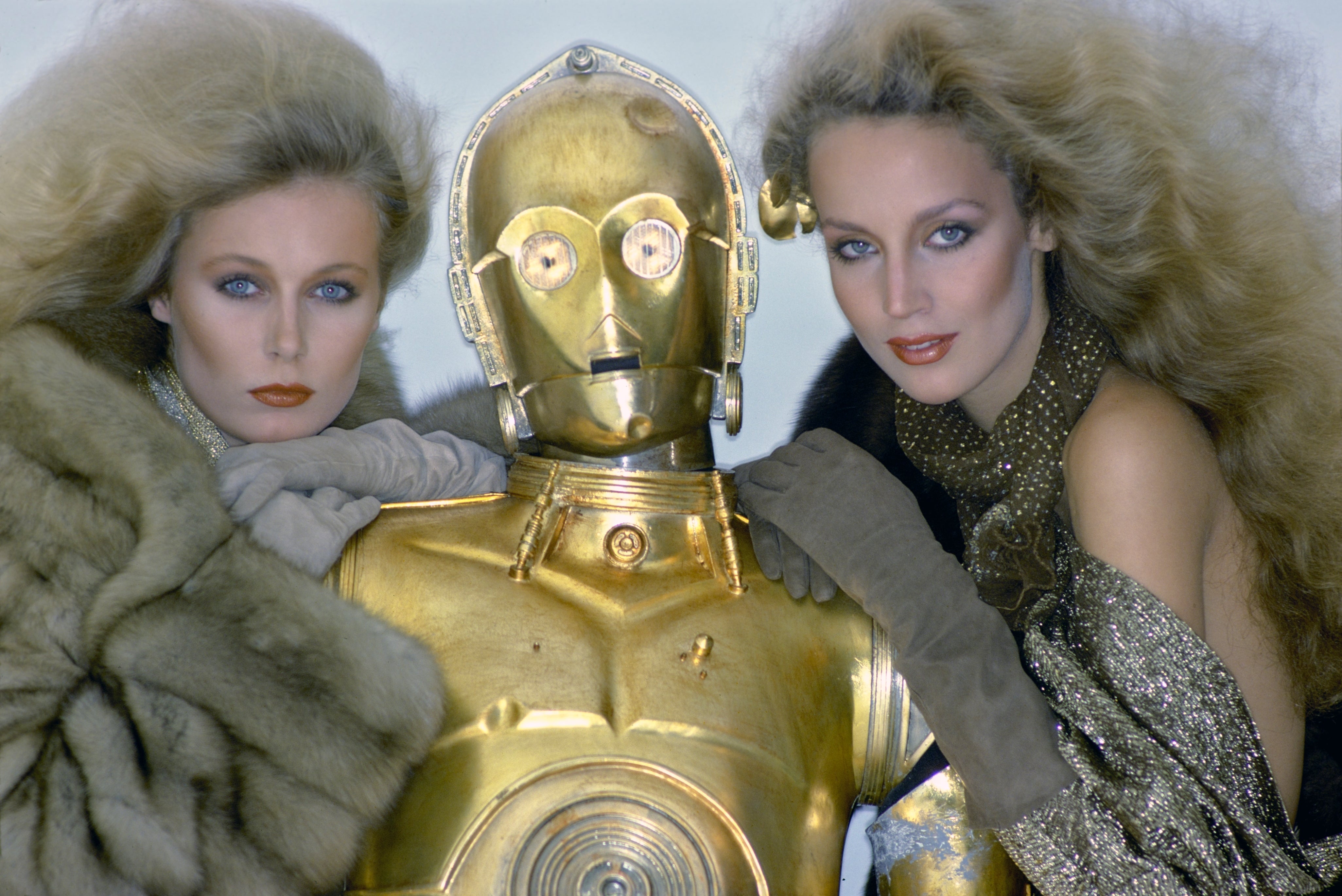 Two women with voluminous hairstyles airs  with a golden  android successful  glamorous, textured outfits