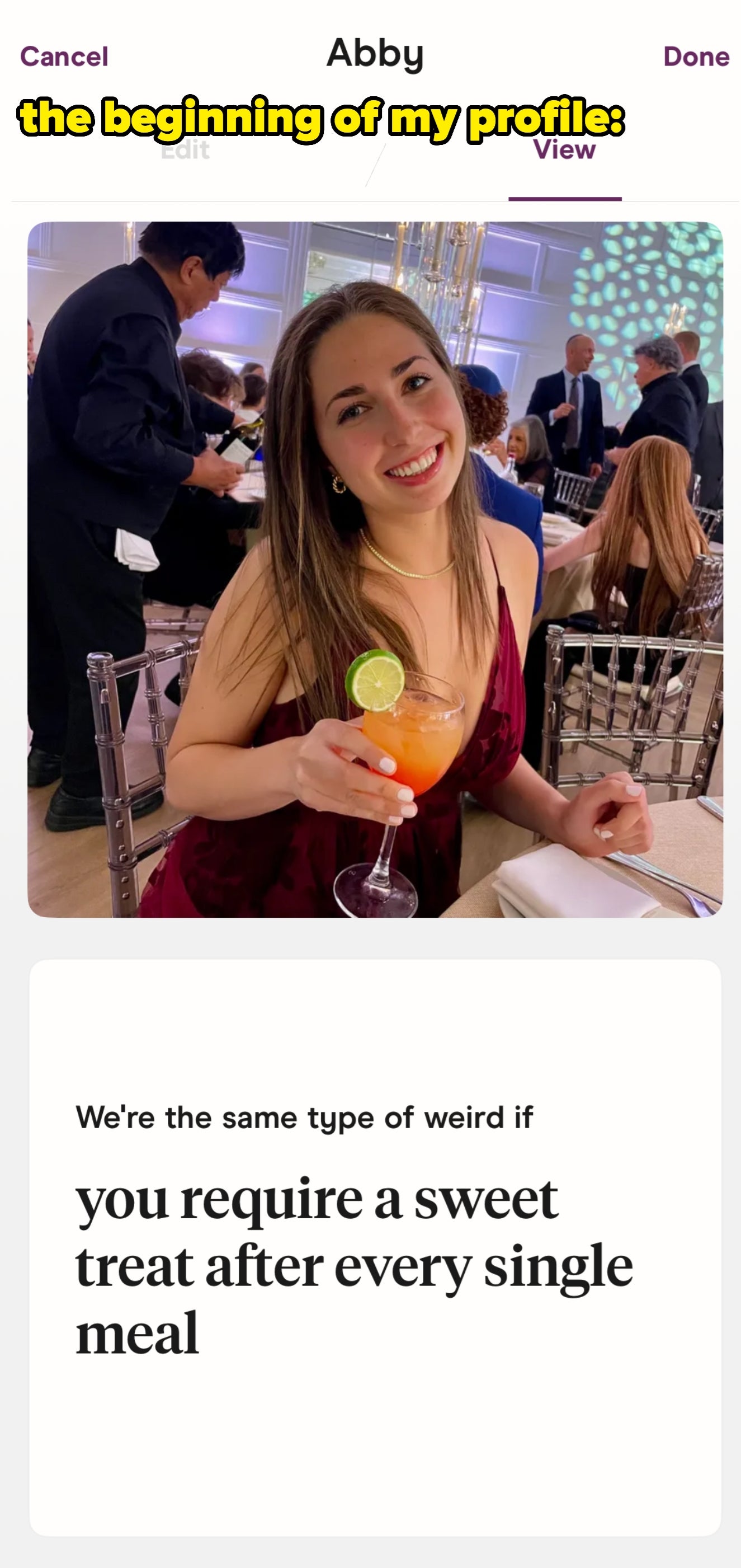En person som smiler, holder en cocktail med en limeskive, sittende ved en formell begivenhet. Teksten nedenfor lyder:
