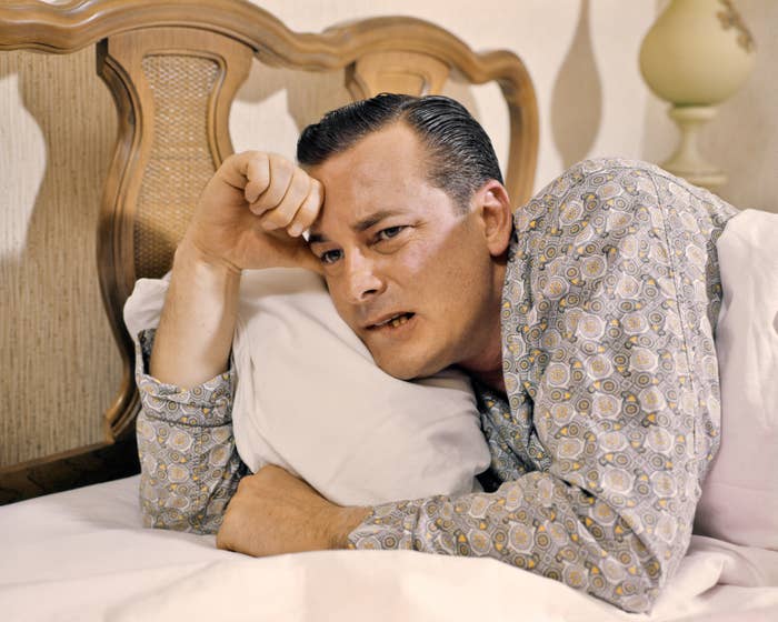 A idiosyncratic   lies connected  a bed, looking thoughtful oregon  concerned, wearing a patterned garment  and resting their caput  connected  a pillow